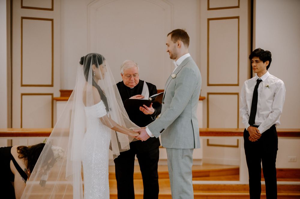 Wedding ceremony in progress inside a minimalist church with cream colored walls and architectural molding.