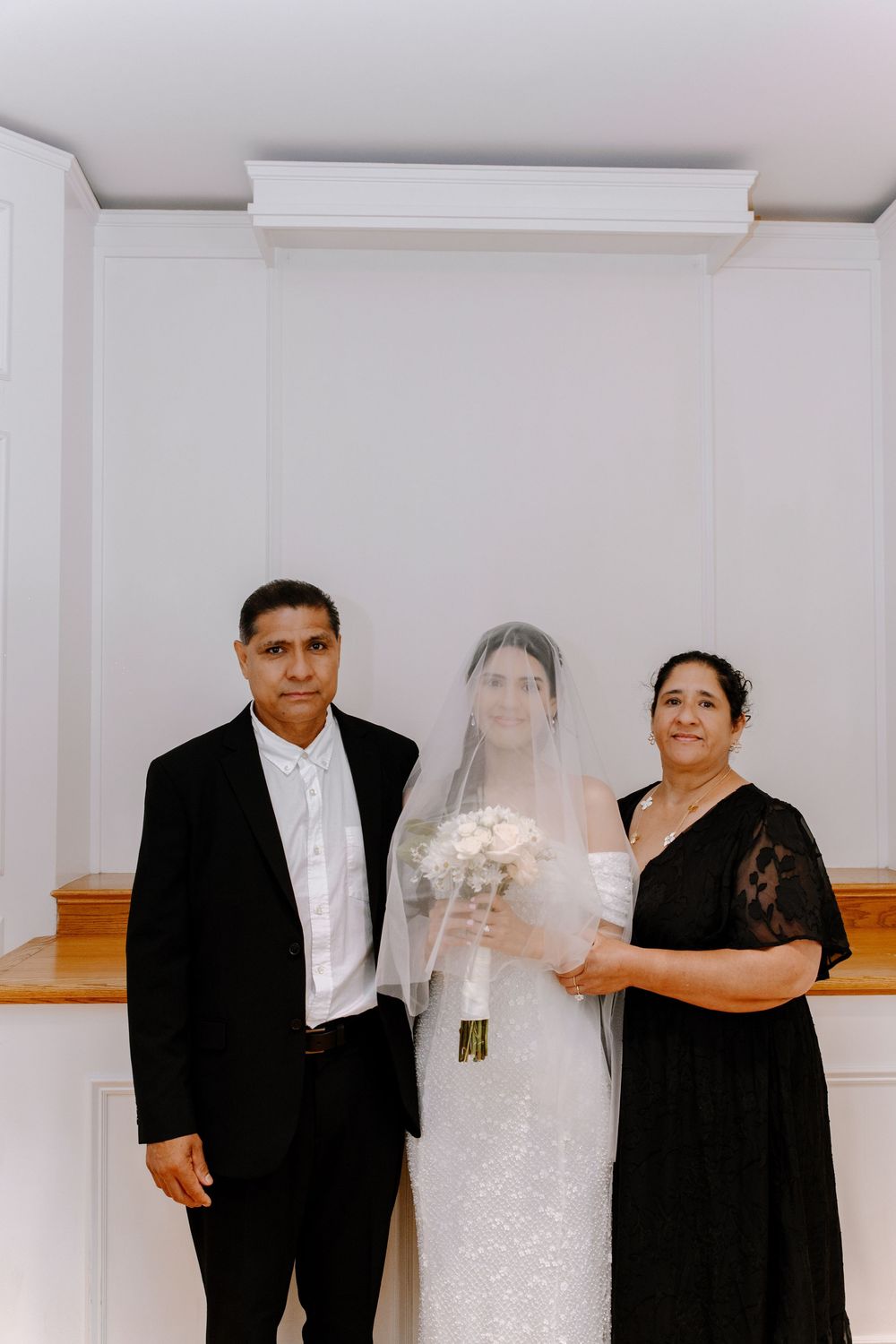 Wedding party members pose in formal attire inside a white-walled interior space during a celebration.