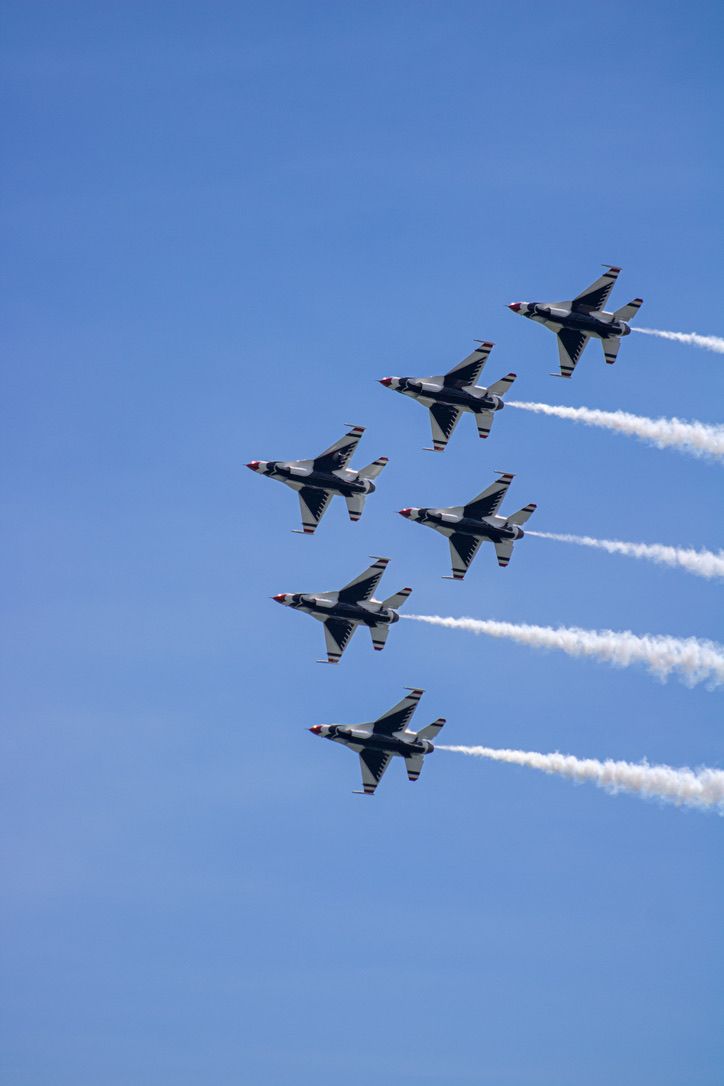 Six military jets flying in formation with white contrails against a bright blue sky.