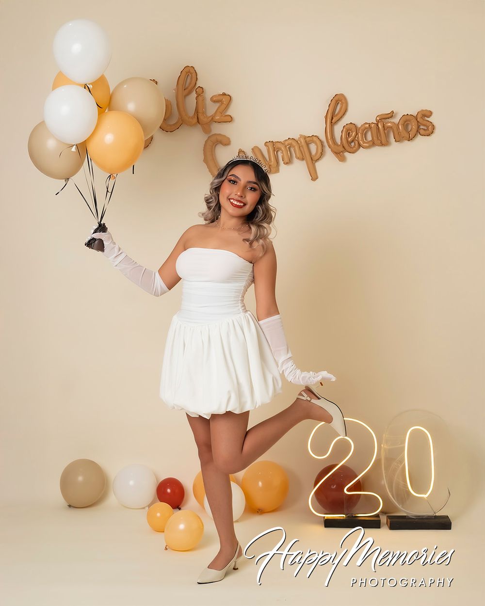 Celebratory photoshoot with white dress and gold lettering decorations against beige backdrop.