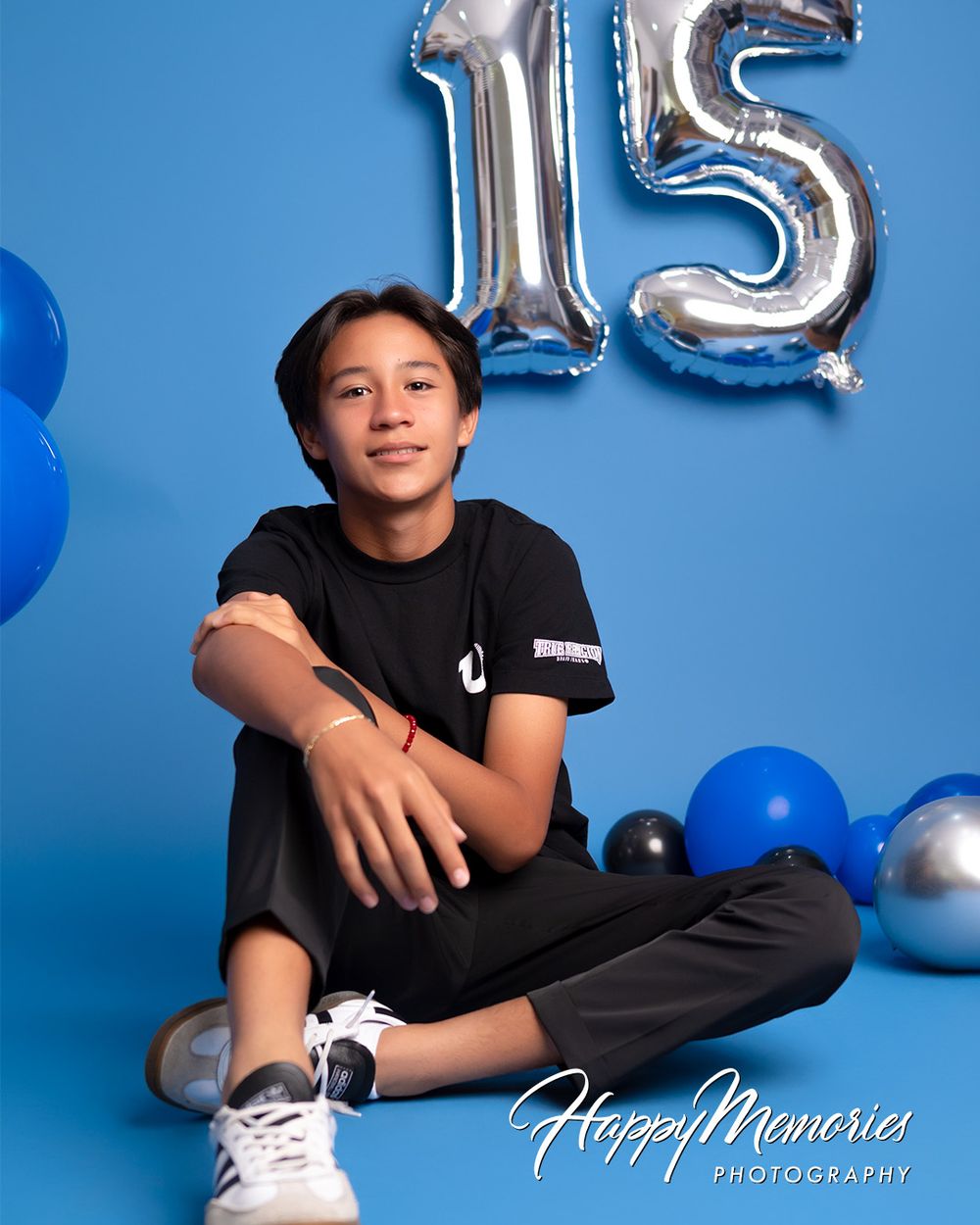 Modern birthday photoshoot with casual black outfit and silver number balloons on blue background.