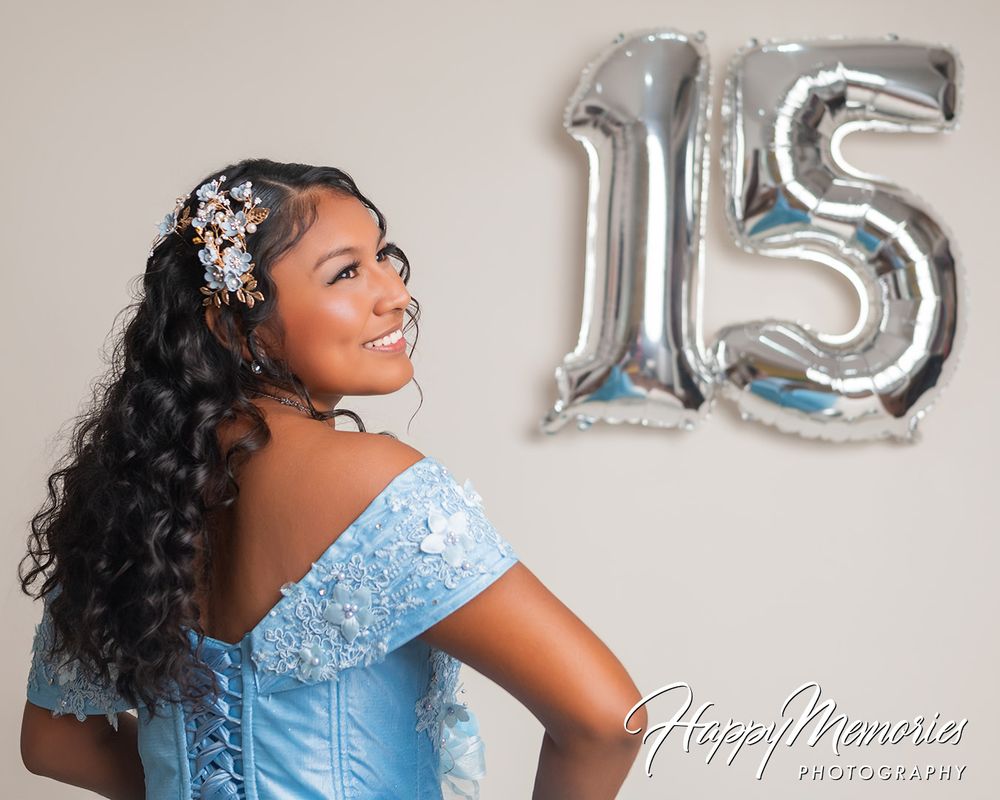 Quinceañera portrait in light blue off-shoulder dress with silver number 15 balloons.