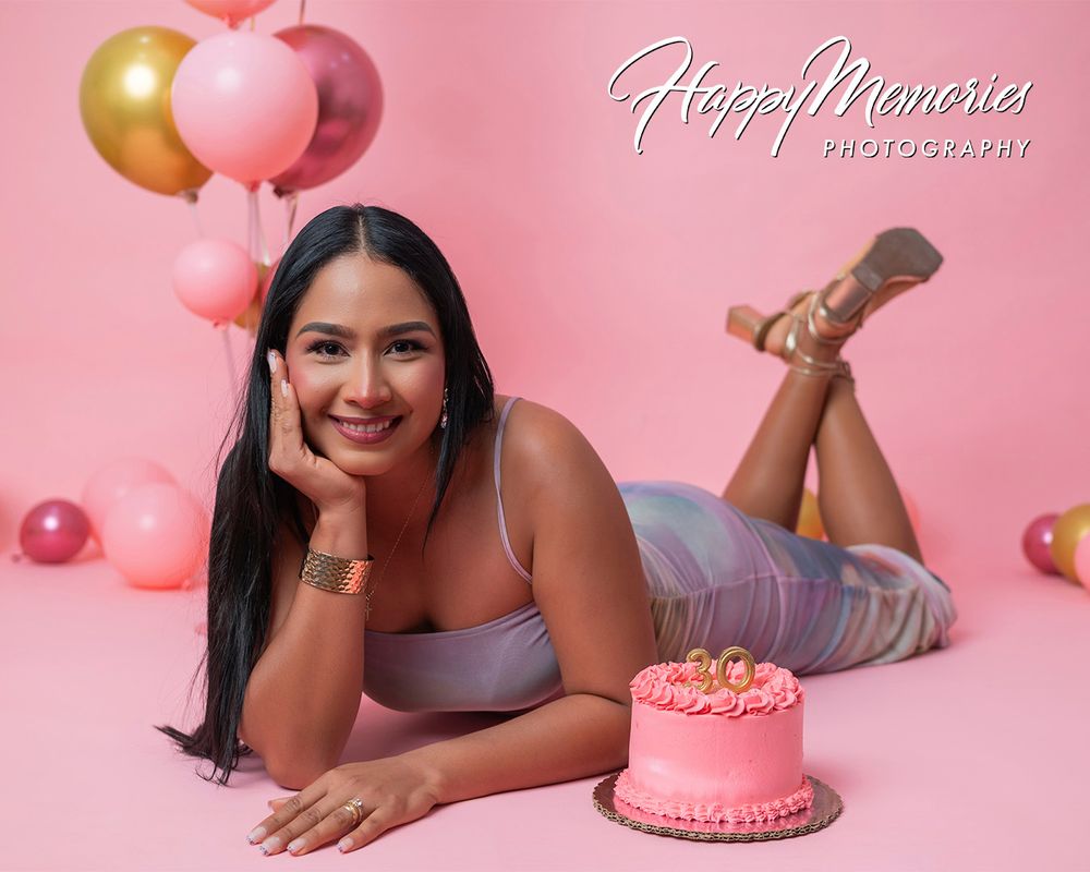 Birthday photoshoot with pink cake and balloons against soft pink background.