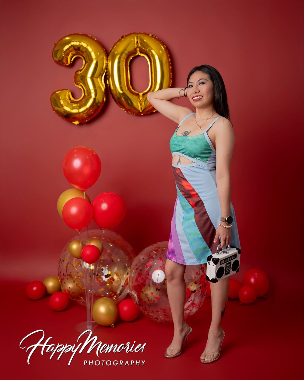 Playful fashion photoshoot with colorful outfits and balloon decorations against red background.