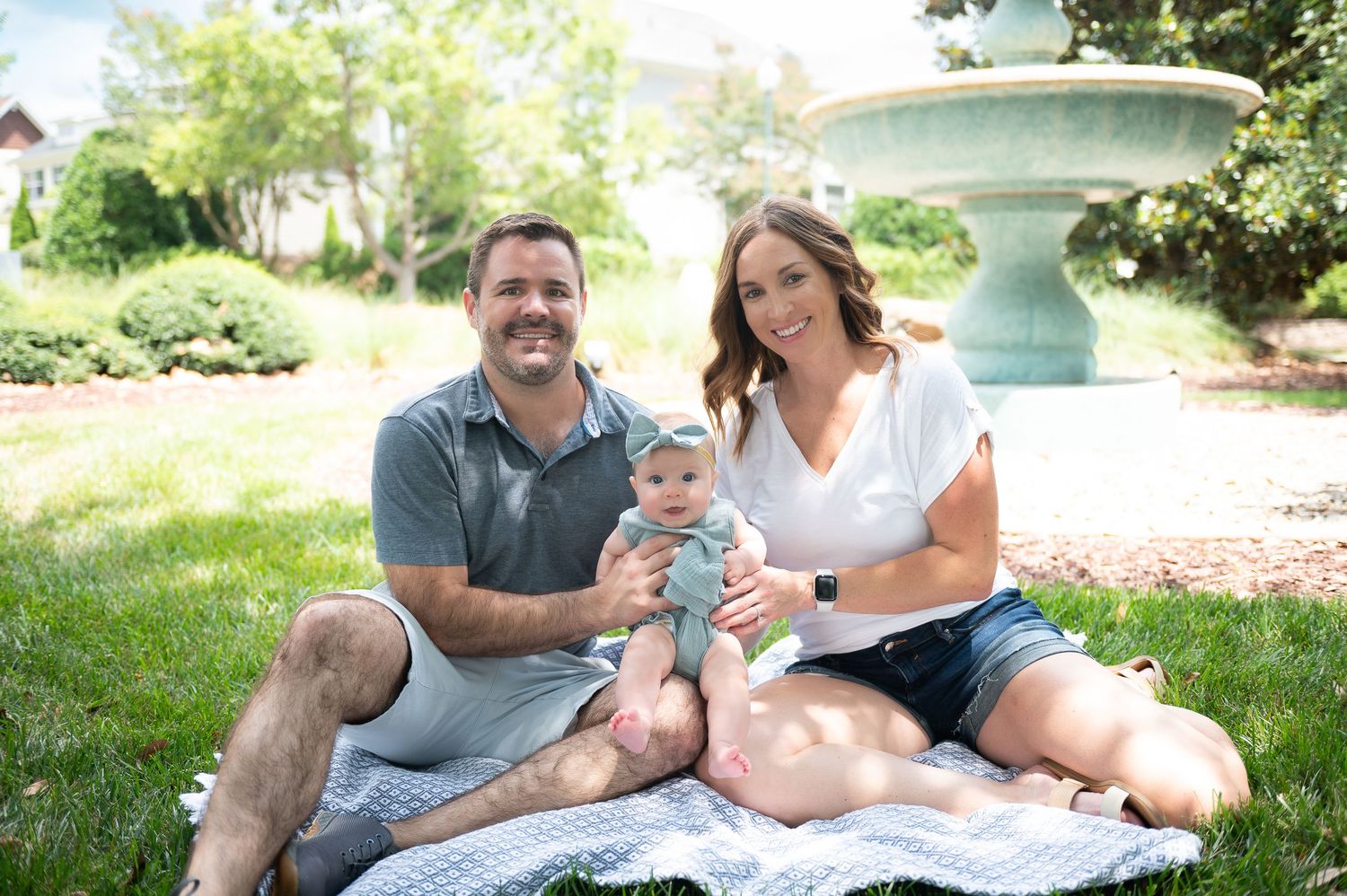 Family relaxing together on green grass under shady trees on a summer day.