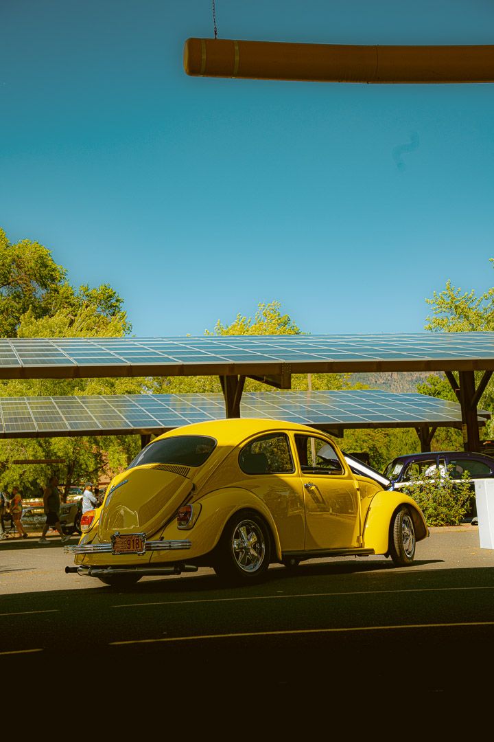 Bright yellow classic Volkswagen Beetles parked under covered solar panel parking showing retro car silhouettes.