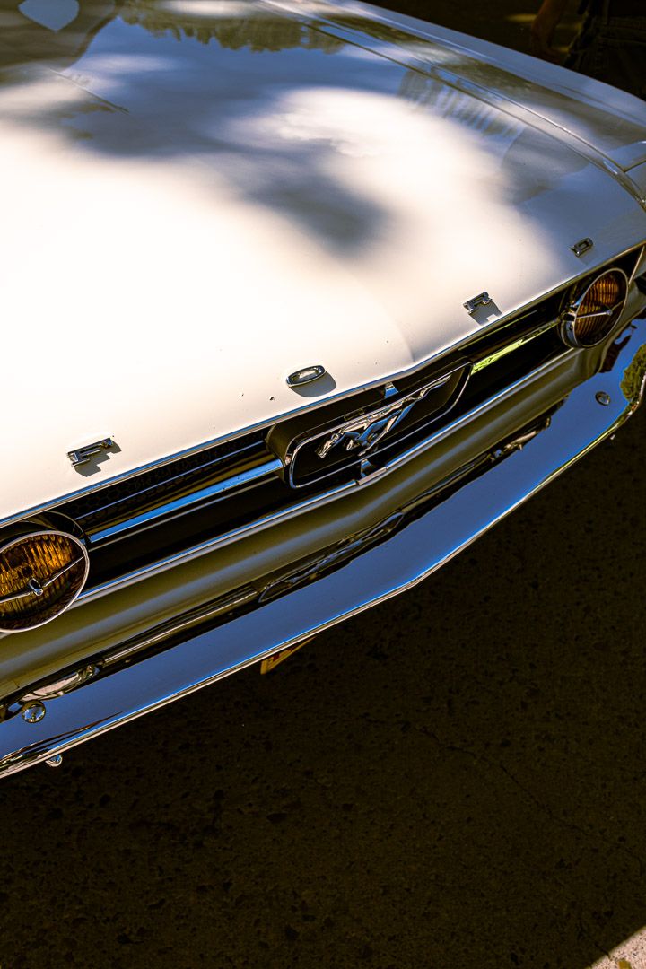 Close-up series showing reflective chrome trim and headlight detail on classic car hood in dramatic lighting.