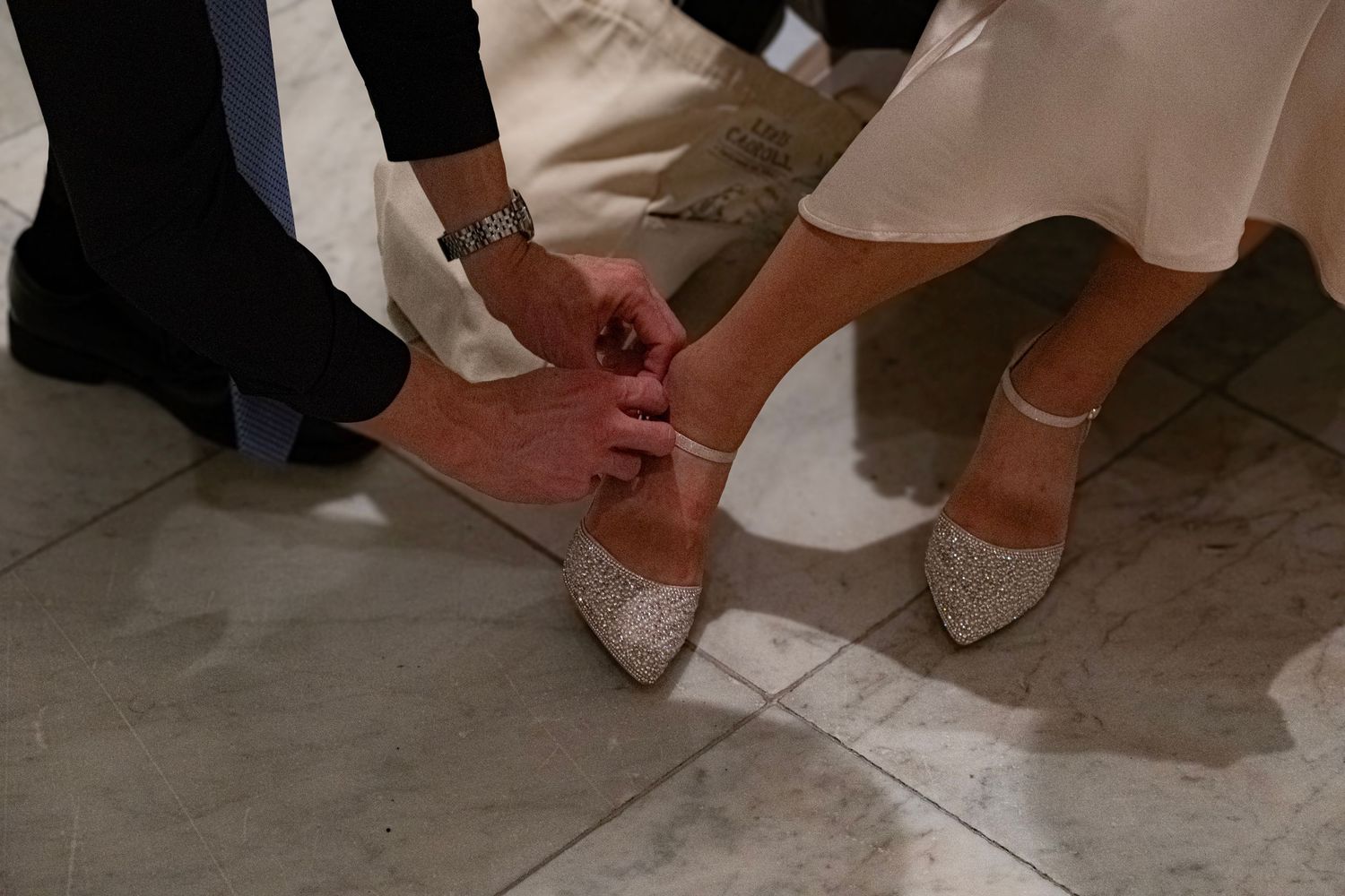 Close-up of formal shoes and dress details on a stone floor.