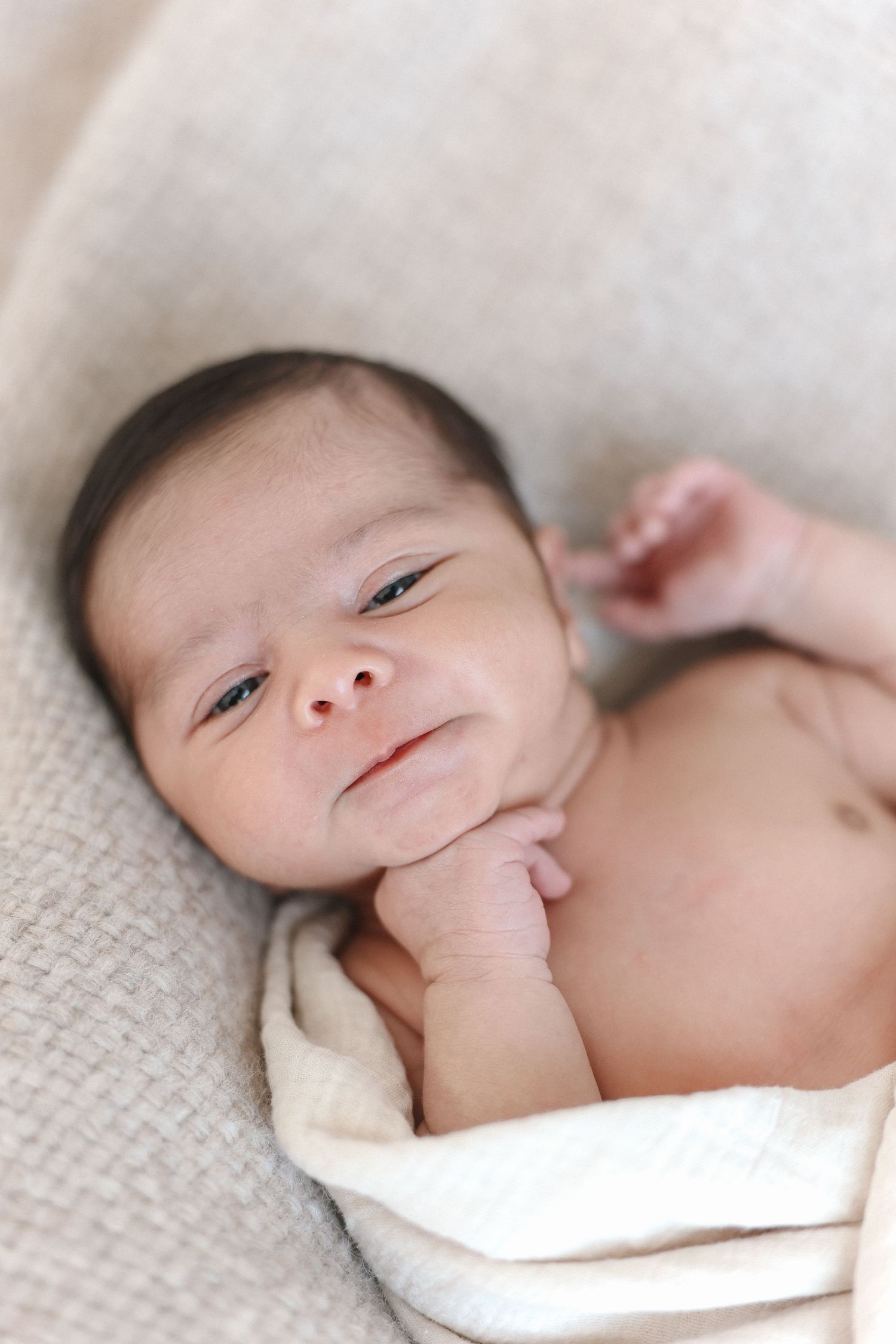 A peaceful newborn baby on soft white blanket with their tiny hand near their mouth and face at Spark Studios Huntington Beach.