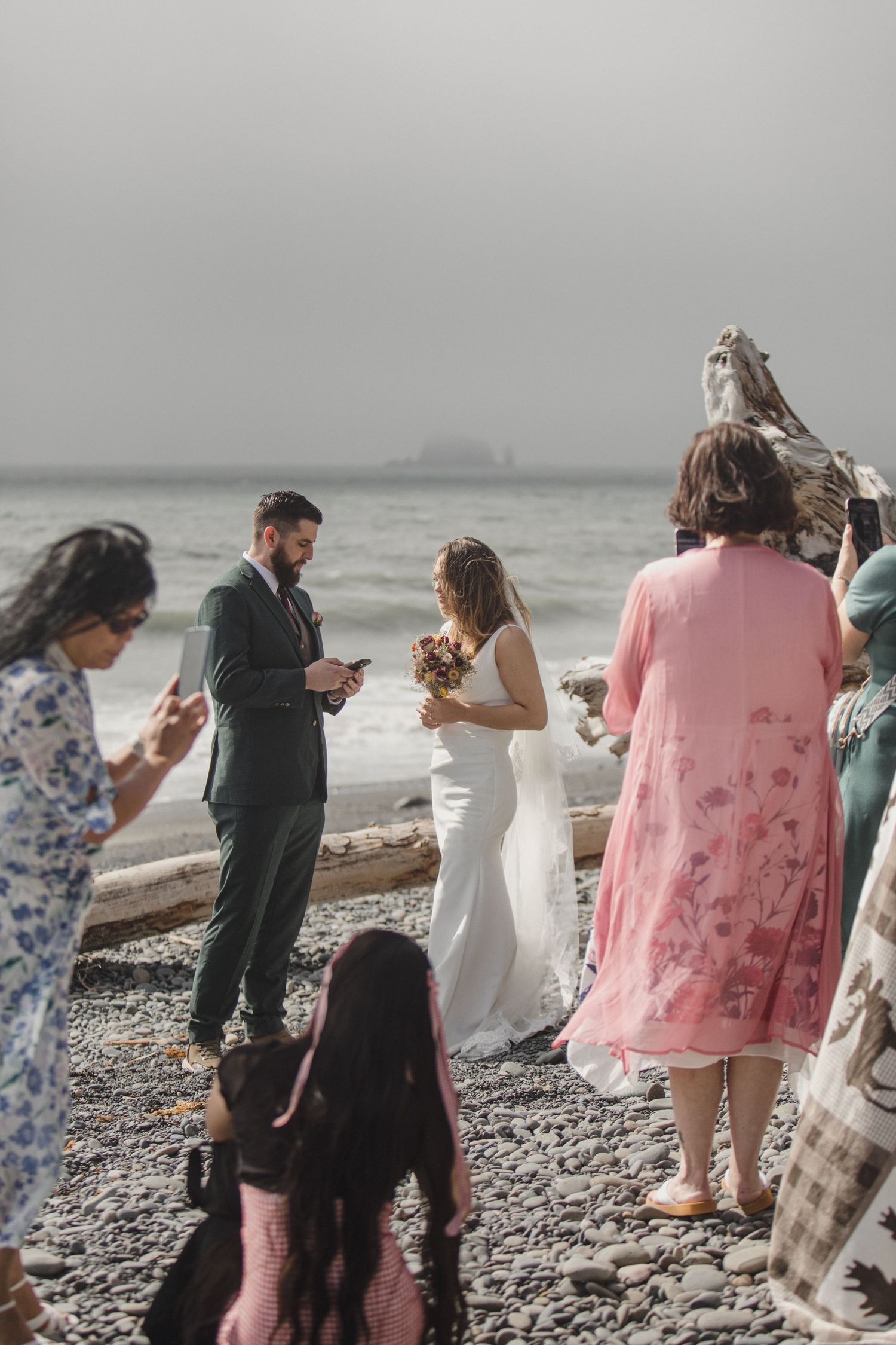 An intimate wedding ceremony on a rocky beach with guests gathered around as vows are exchanged.