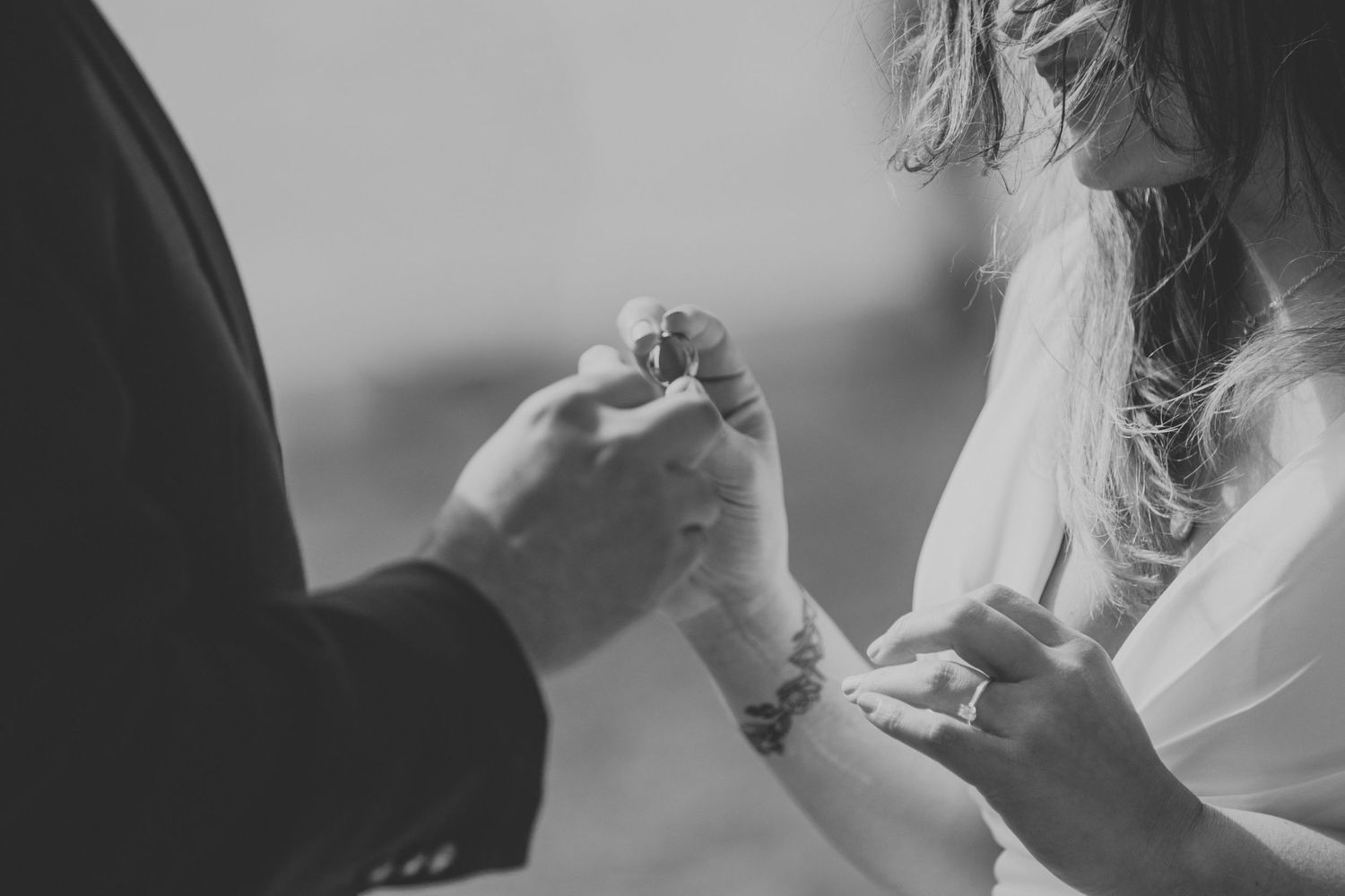 A close-up black and white shot of hands exchanging rings during a wedding ceremony.