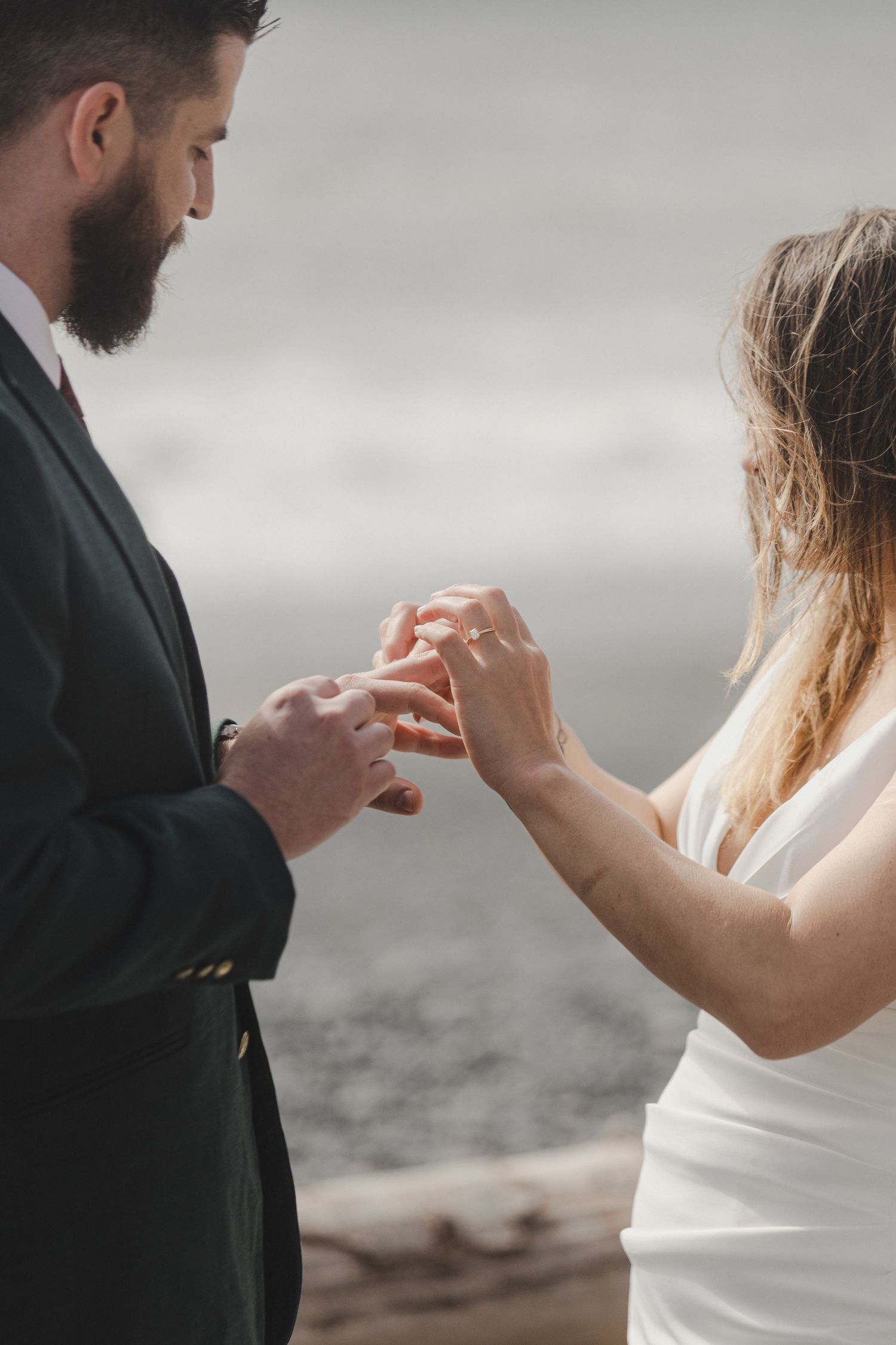 Close-up of bride and groom exchanging rings during outdoor wedding ceremony against cloudy backdrop.
