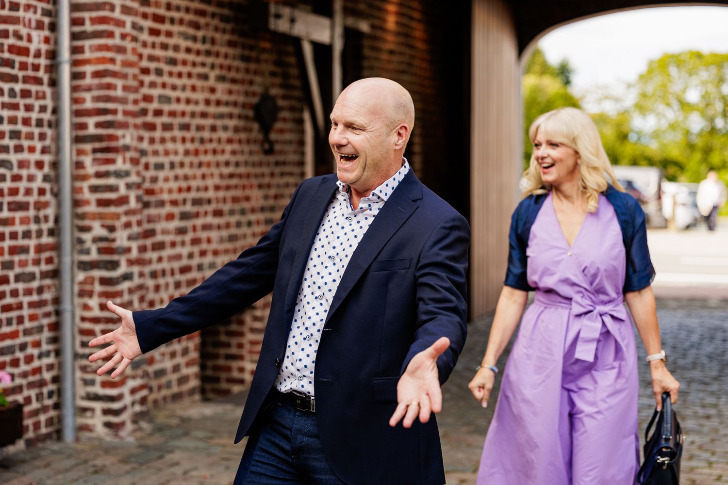 A couple shares a joyful moment during what appears to be an engagement photoshoot against a brick wall background.