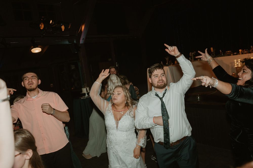 Bride and groom dancing joyfully with guests at lively wedding reception under dark sky.