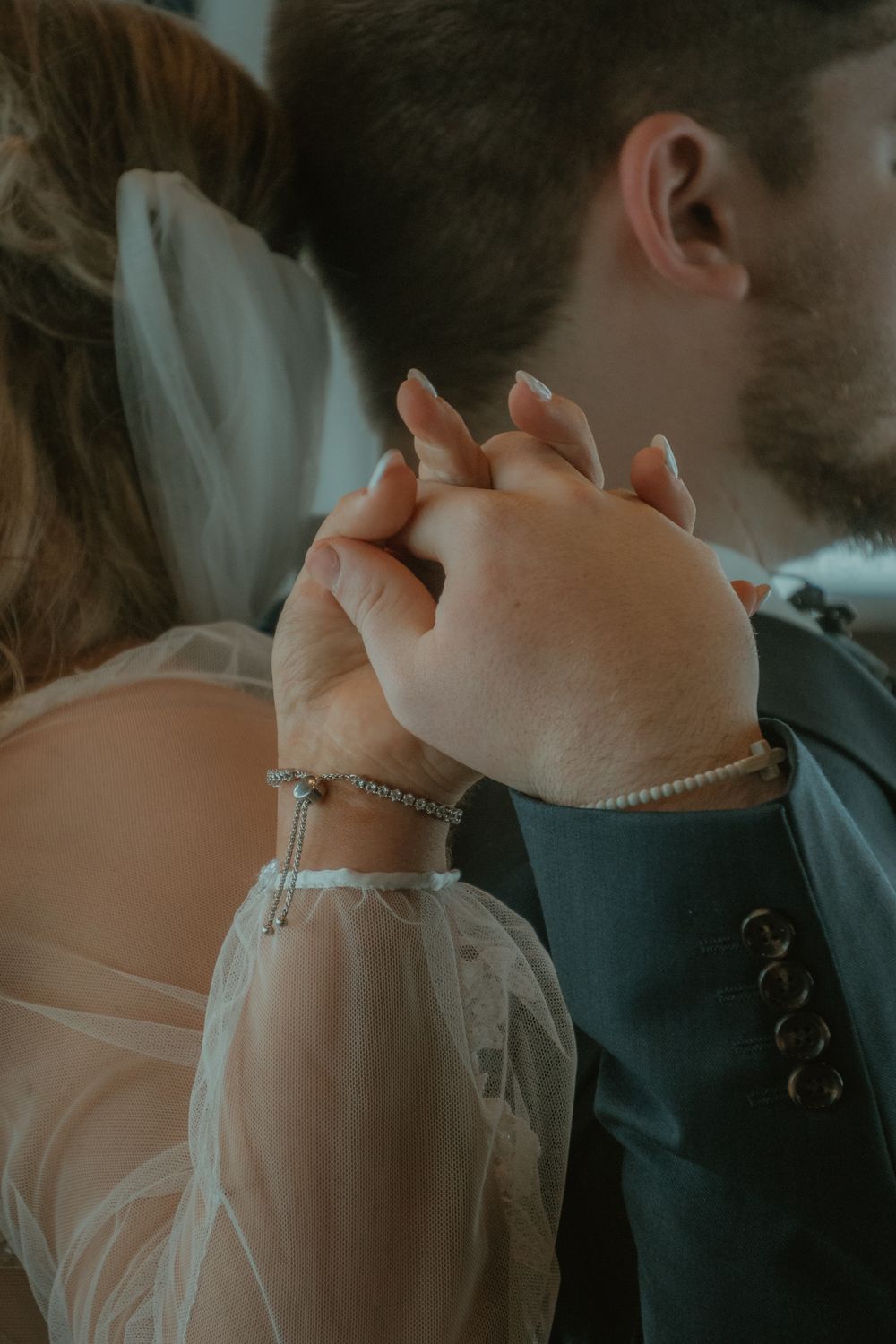 Close-up of bride and groom holding hands, bride wearing diamond bracelet and pearl bracelet.