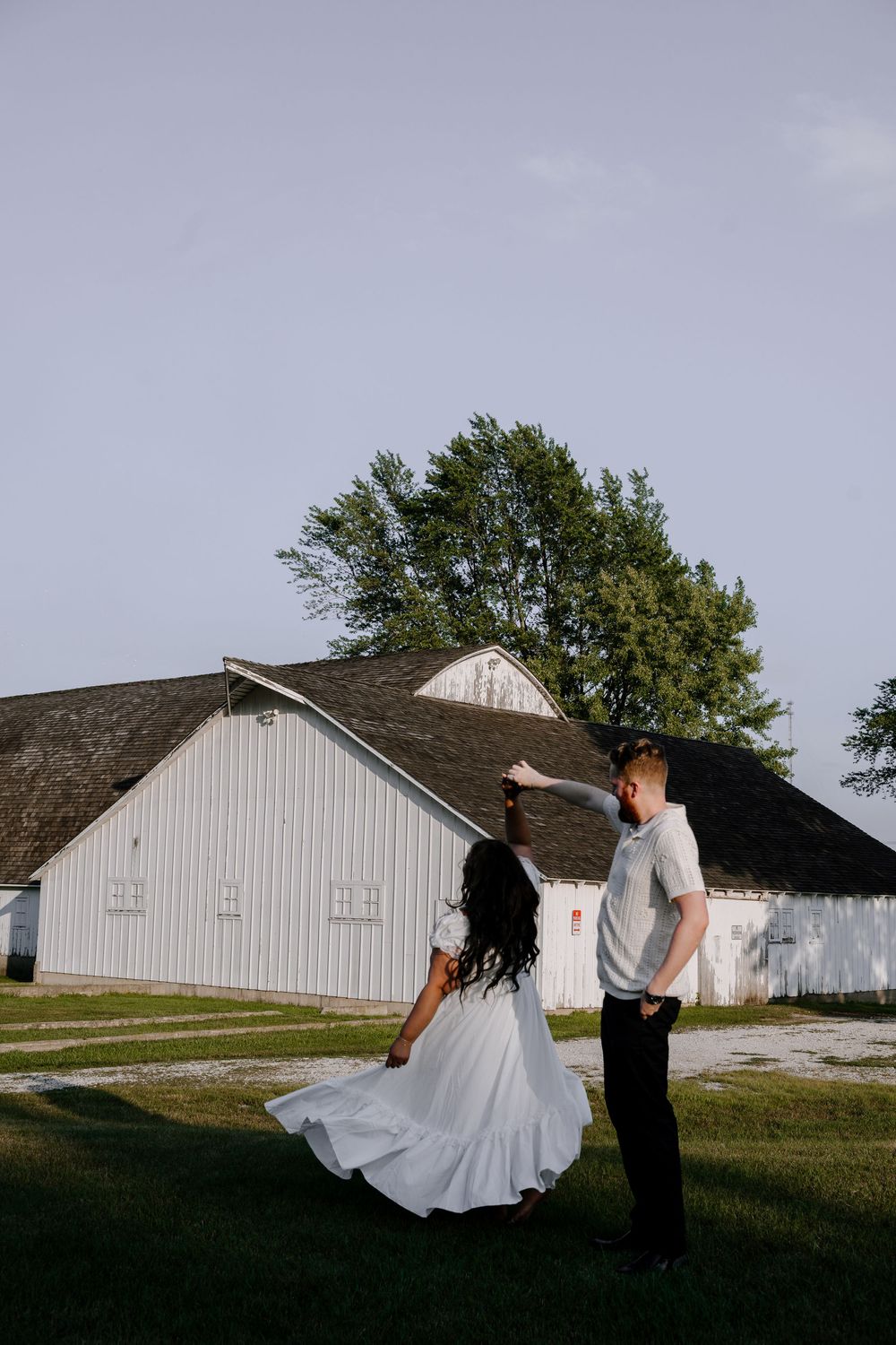 Dancing couple spins gracefully against the backdrop of a white farm building.