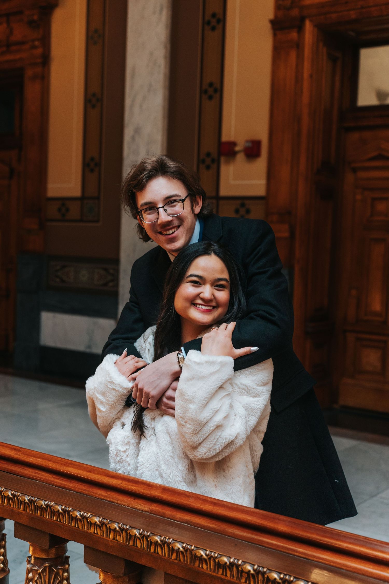 Couple sharing joyful moment on ornate wooden staircase in historic building.