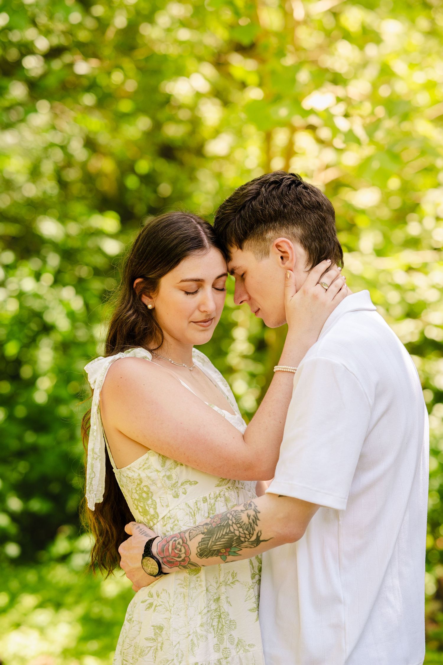 Couple embraces tenderly in a garden setting with soft green bokeh background on a sunny day.
