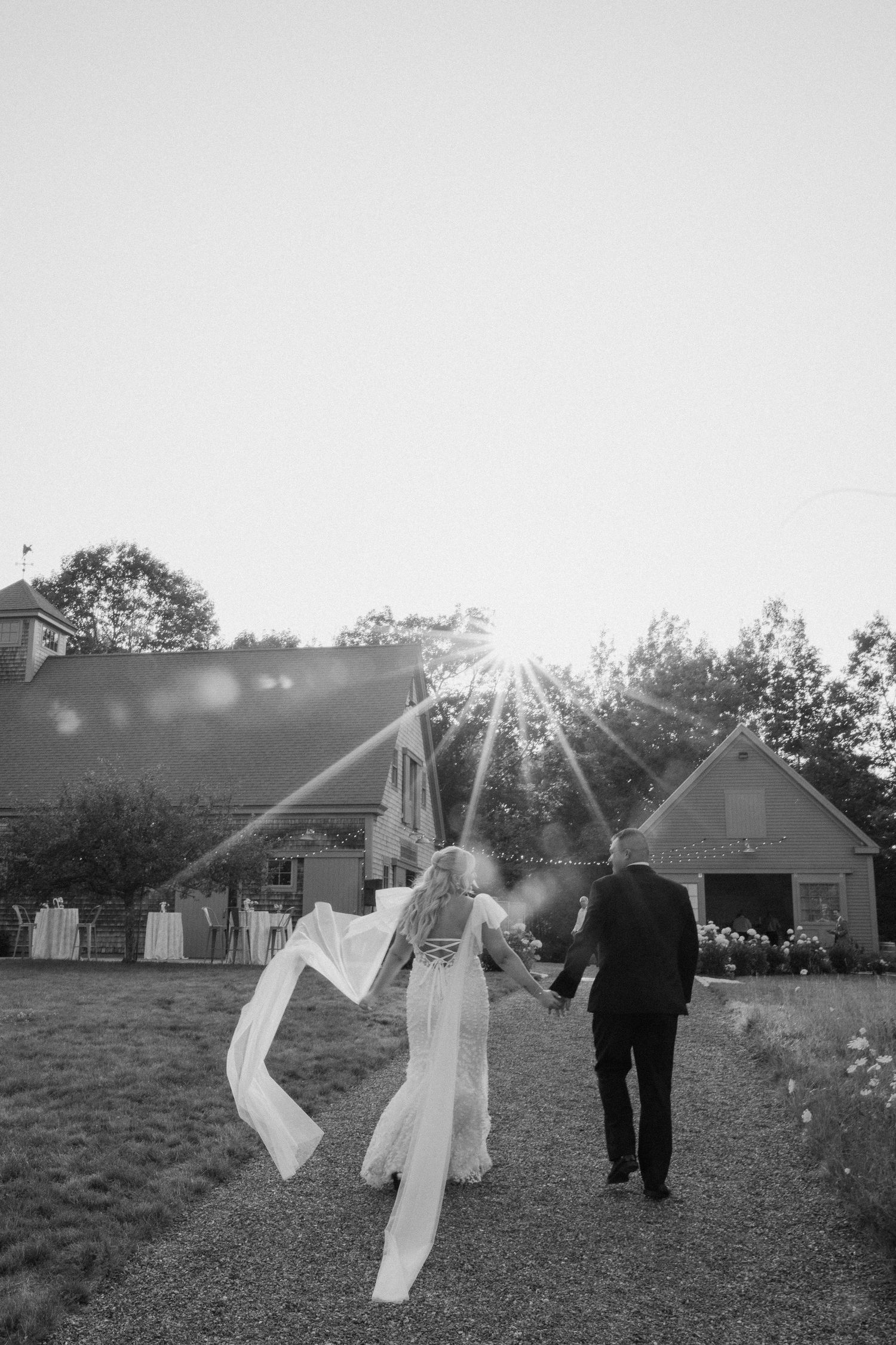 A couple walks through a field at sunset with white fabric flowing in the breeze.