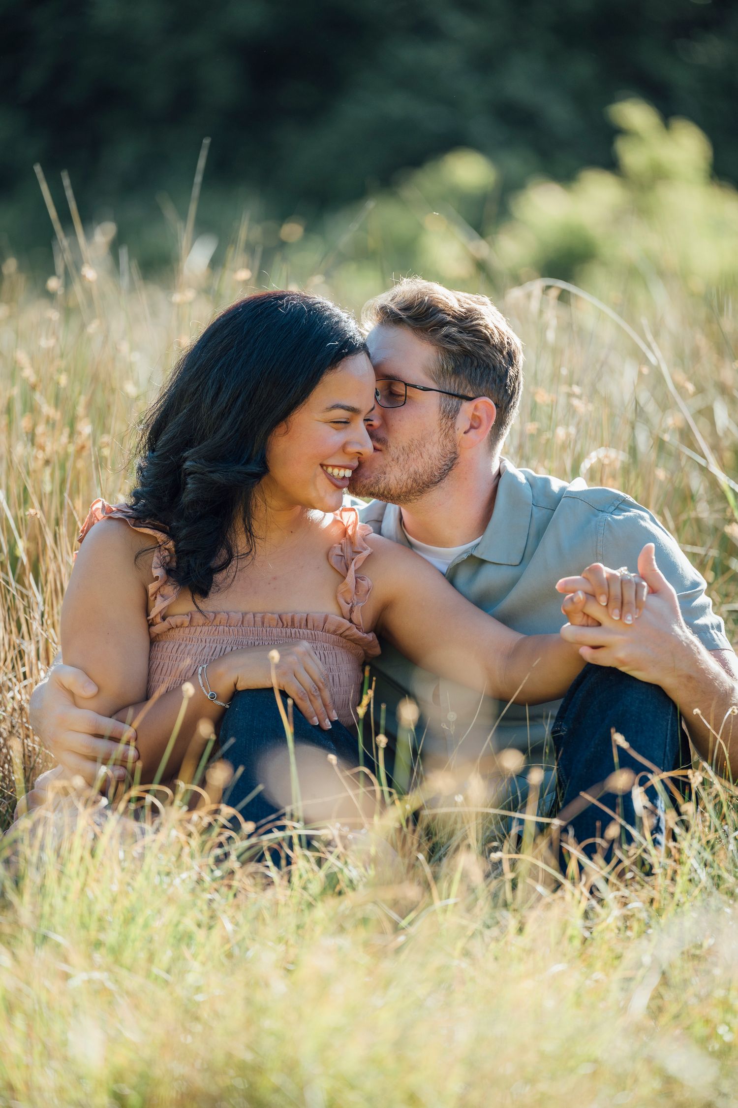 A romantic couple shares an intimate moment while sitting together in a sunlit meadow of tall golden grass.