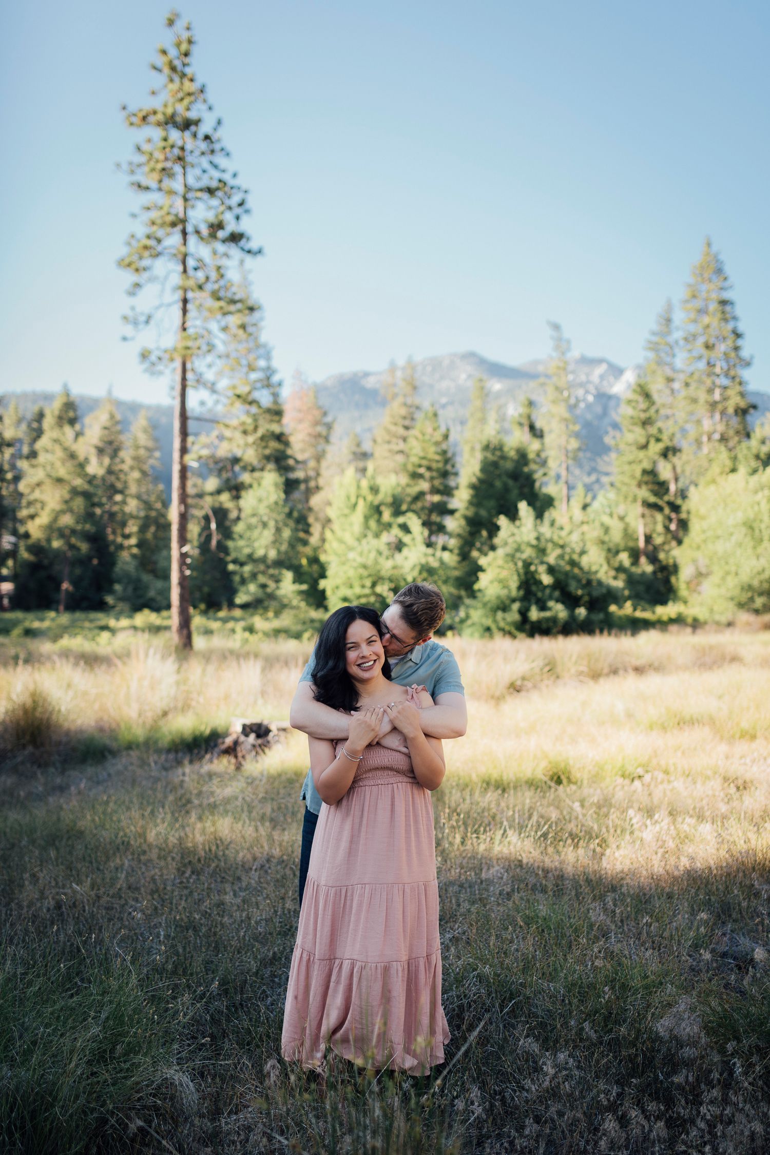 A scenic mountain engagement photo session in the evening light with pine trees and a meadow in the background.