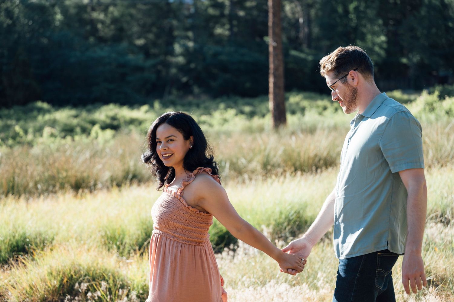 Person wearing jeans and white shirt leads their partner in a dance outdoors in a grassy field at sunset.