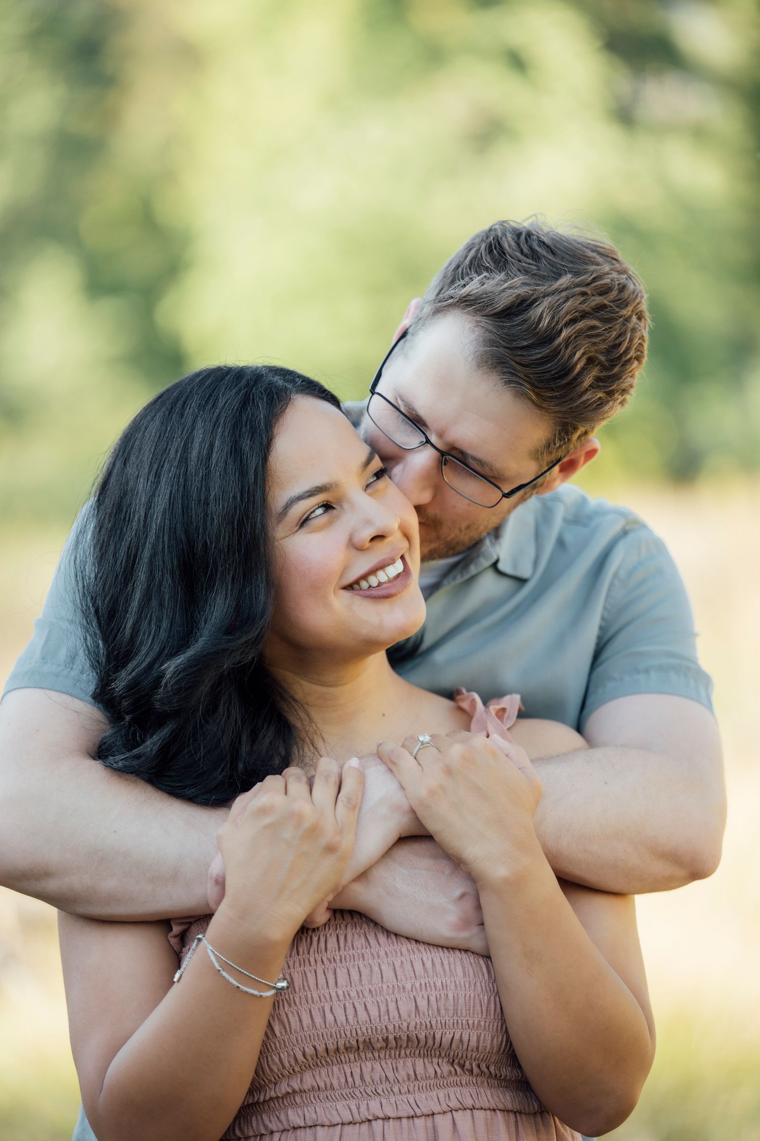 A romantic portrait of a couple embracing outdoors with natural bokeh background in warm sunlight.