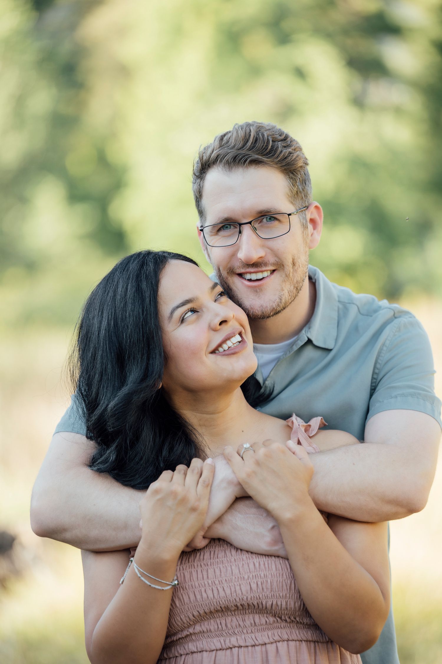 Happy couple embraces outdoors with natural sunlit backdrop during romantic photoshoot in the park.