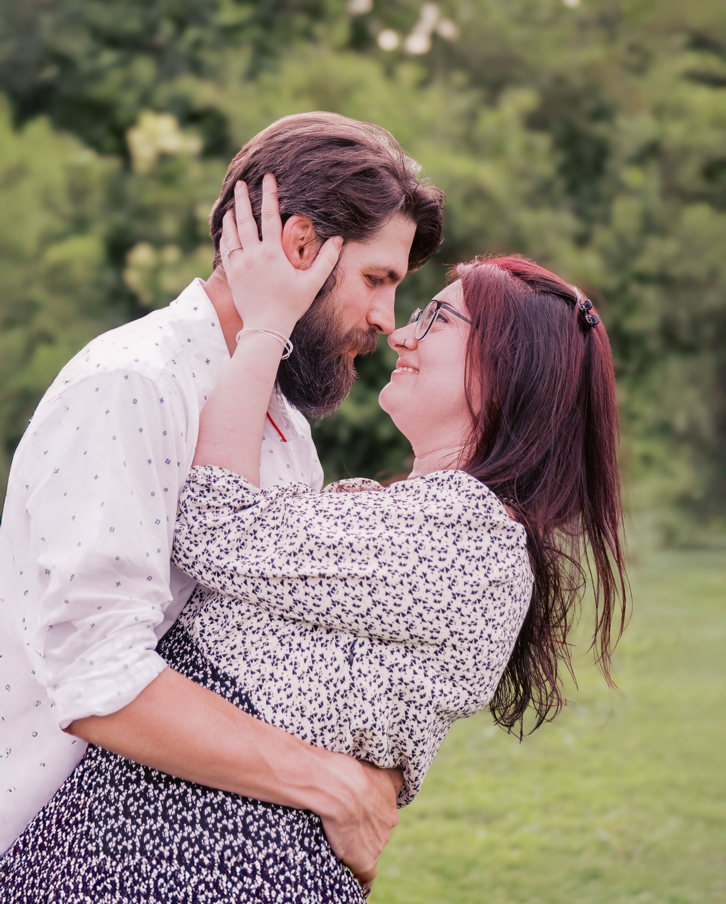A romantic couple embraces in a garden setting wearing casual attire.