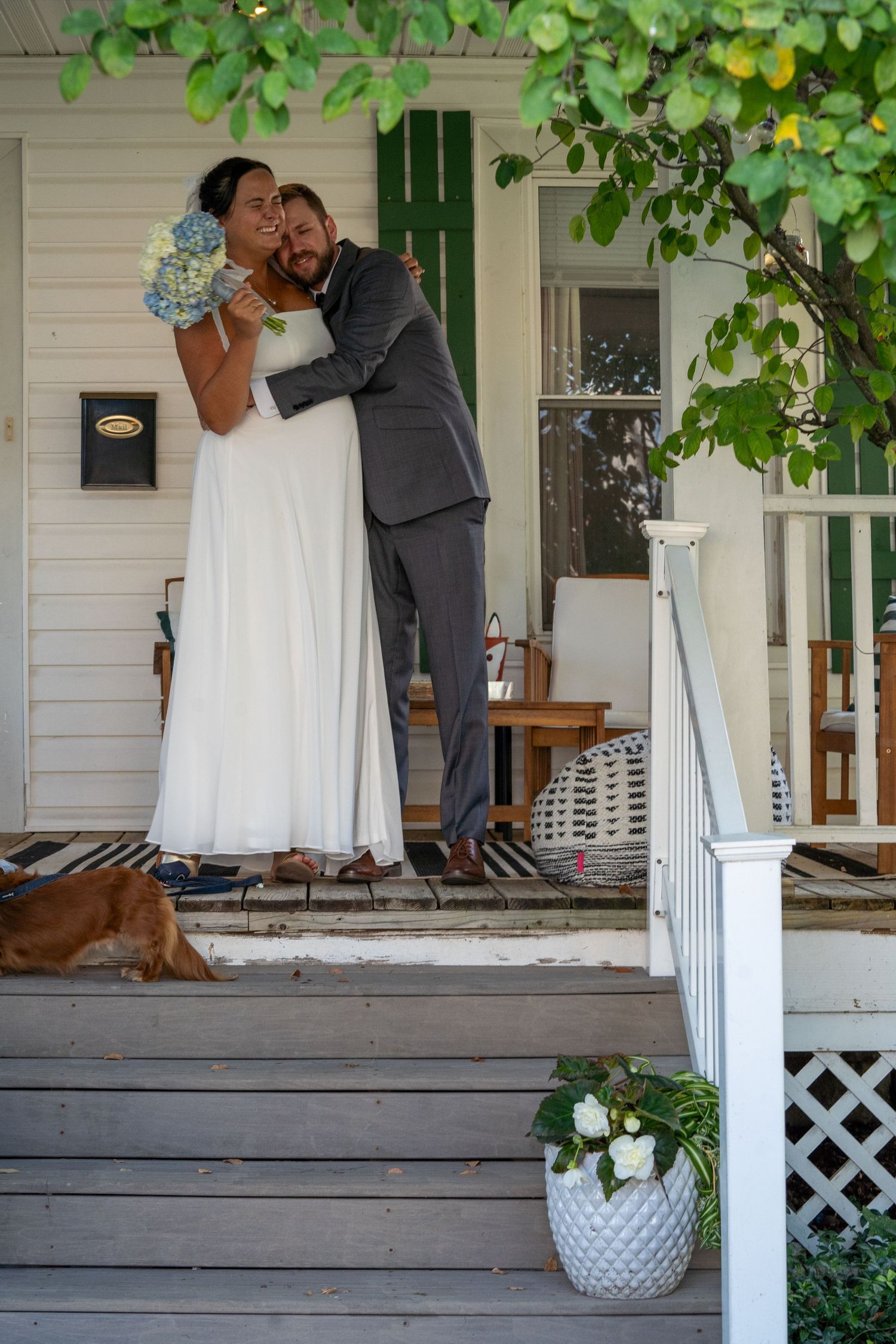 A wedding photoshoot on a charming white porch with wooden details and green foliage.