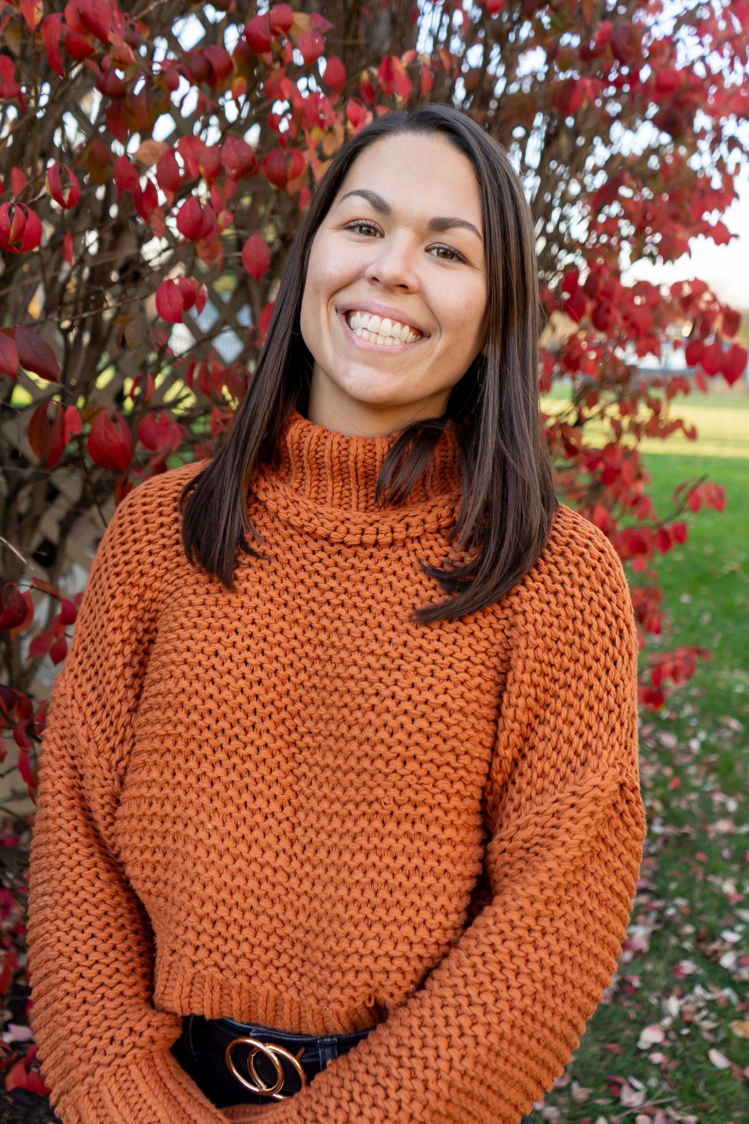 A chunky knit orange turtleneck sweater photographed against red autumn leaves.