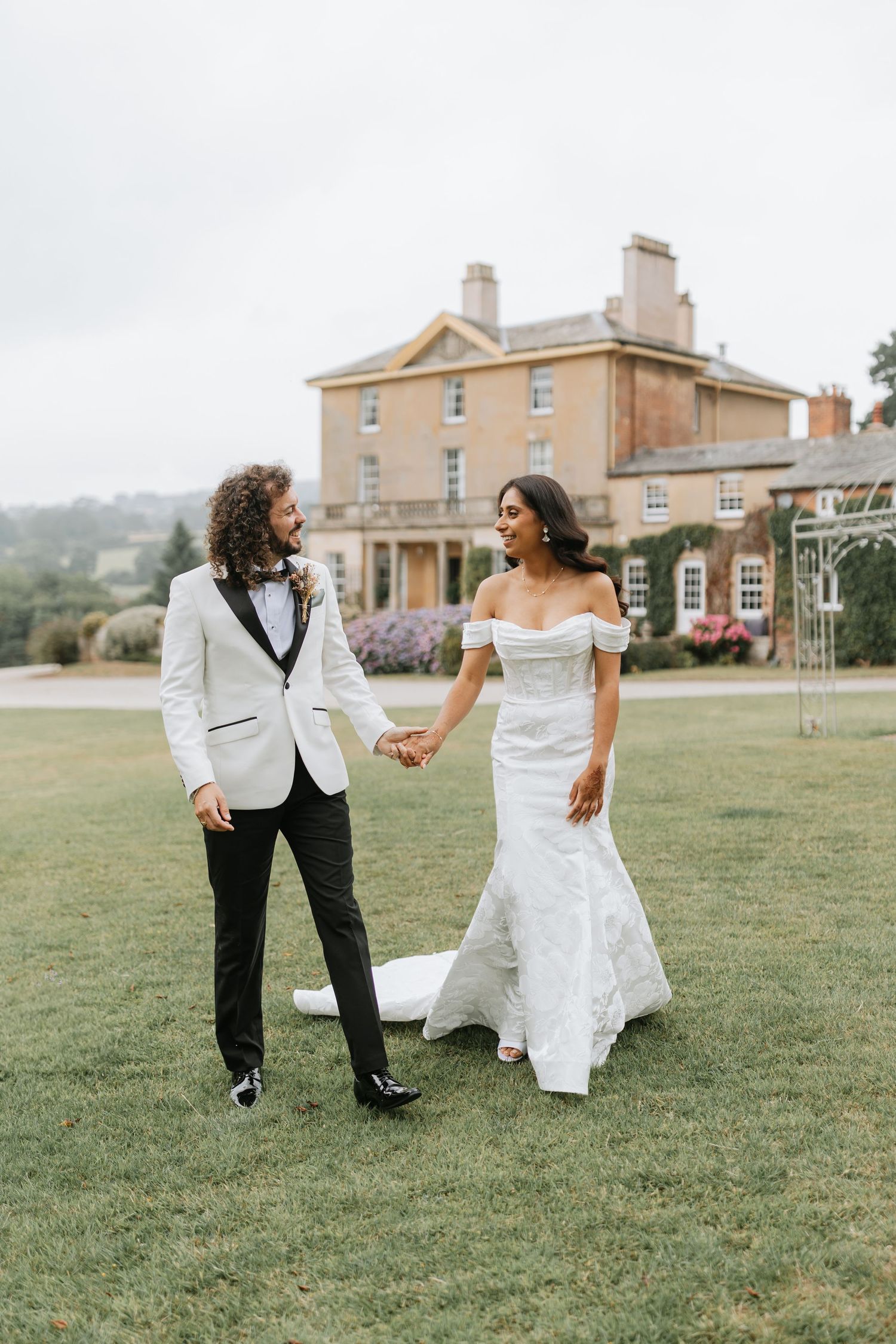 Couple dancing and twirling on a grassy lawn with an elegant manor house in the background in romantic wedding photography. Hopton Court