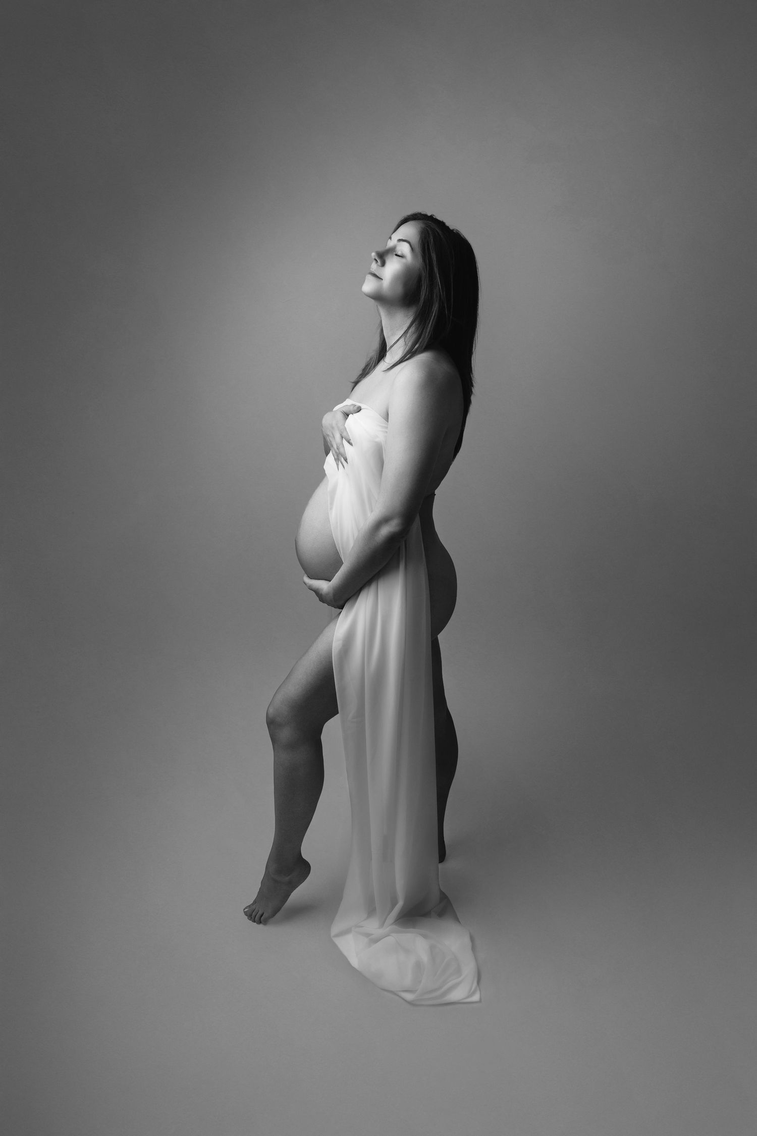 Artistic black and white maternity photos showing a pregnant woman in a flowing white dress.