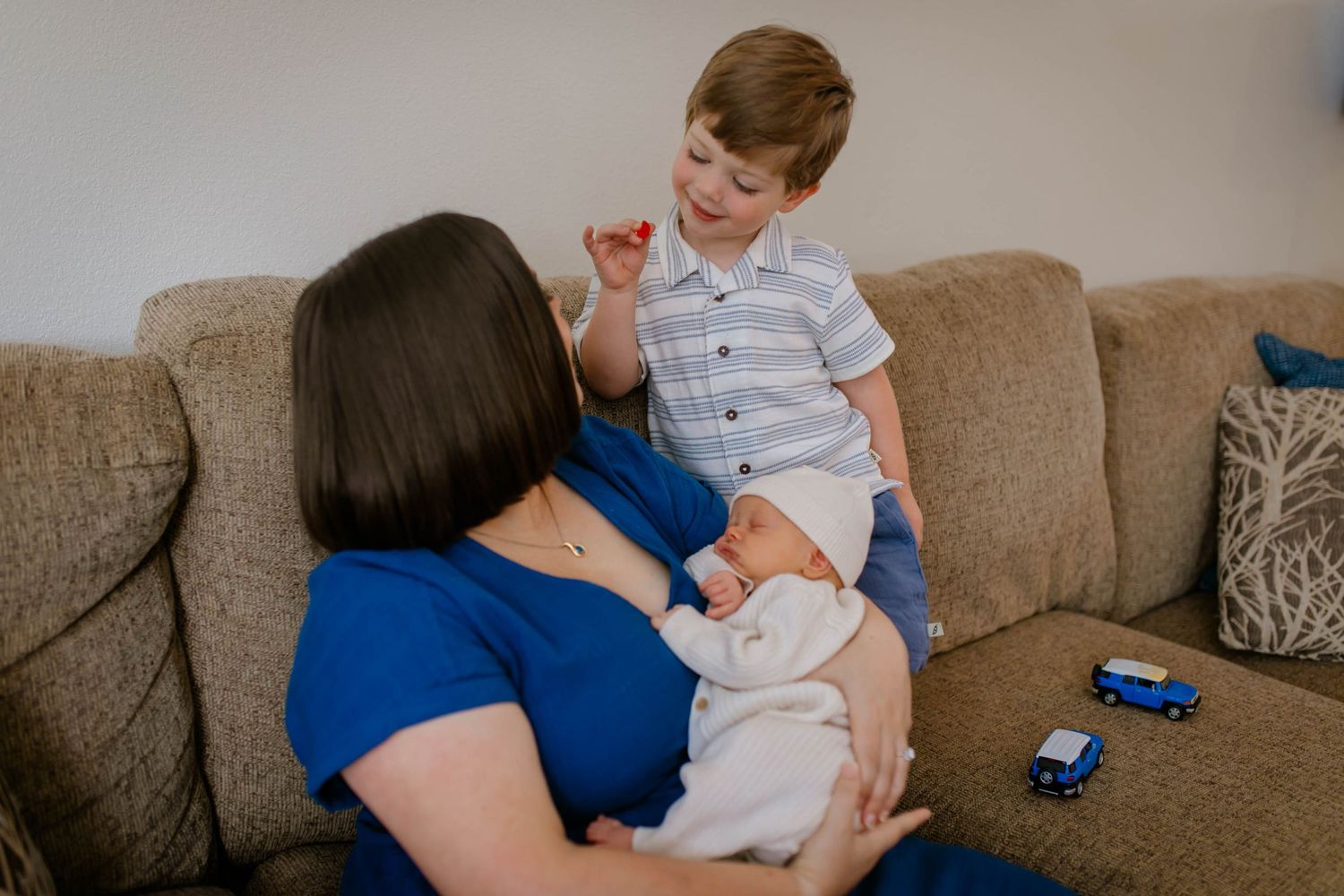 Parent and child sharing a tender moment while sitting on a brown couch with toy cars visible nearby.