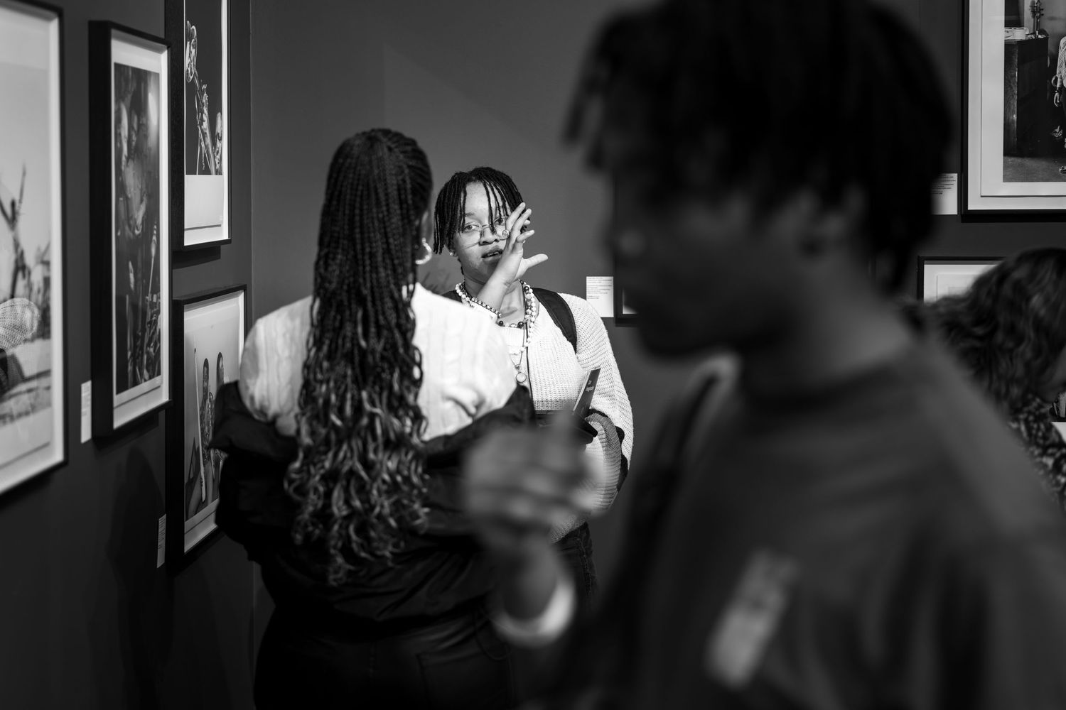 Black and white portrait photograph showing people talking and socializing at what appears to be an art gallery or exhibition.