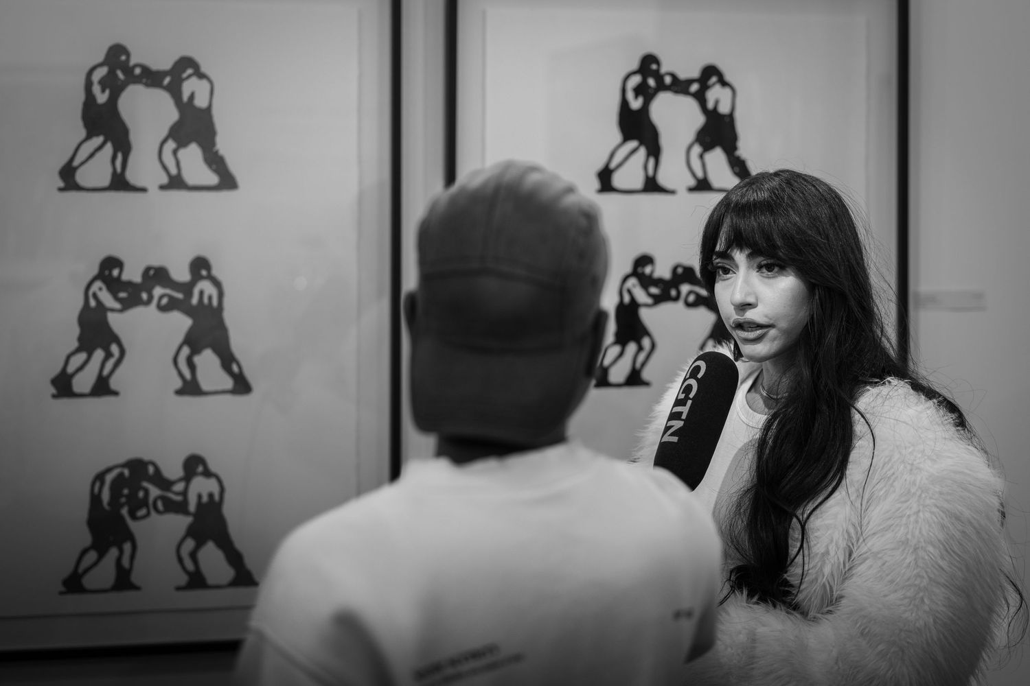 A black and white photograph showing silhouettes of wrestlers on a wall while two people converse in the foreground.