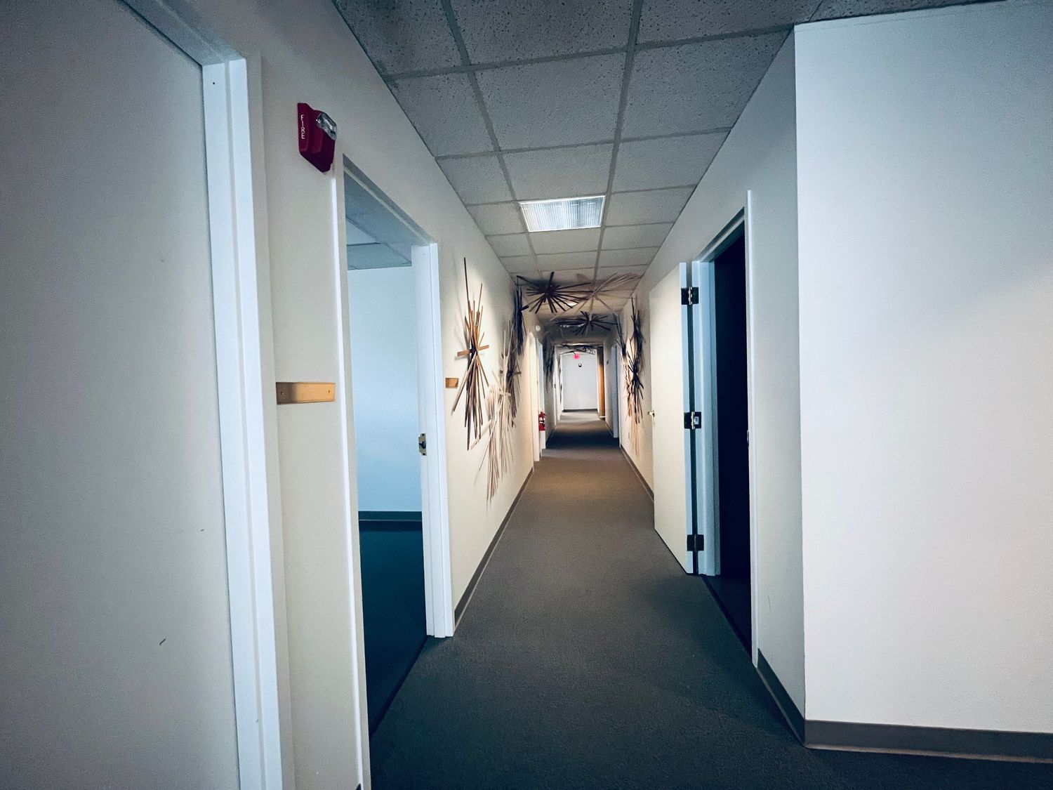 Long white hallway with fluorescent lighting and blue doors stretches into the distance showing institutional interior design.