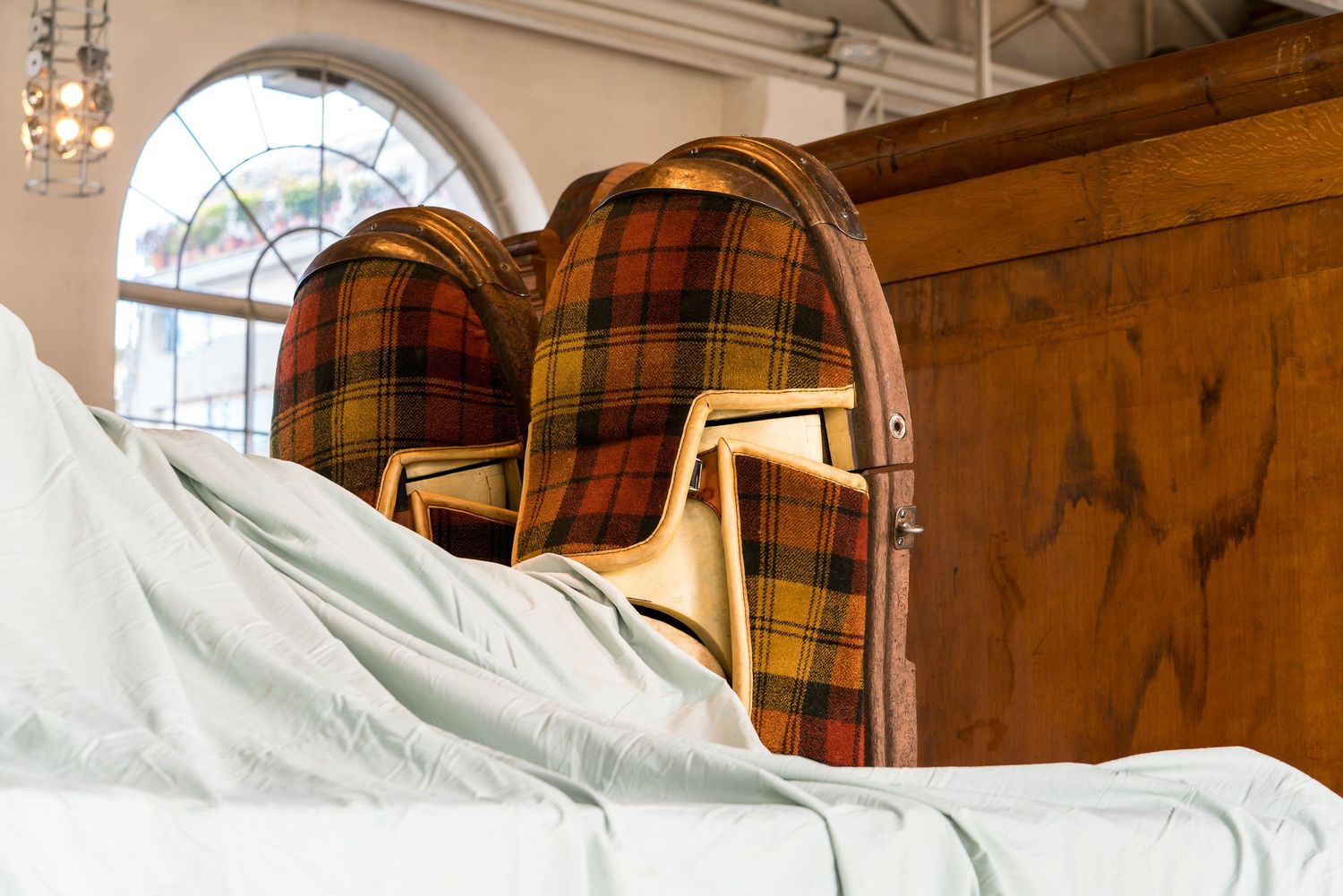 Rustic bedroom with wooden beams, white bedding, and an arched window displaying warm natural lighting.