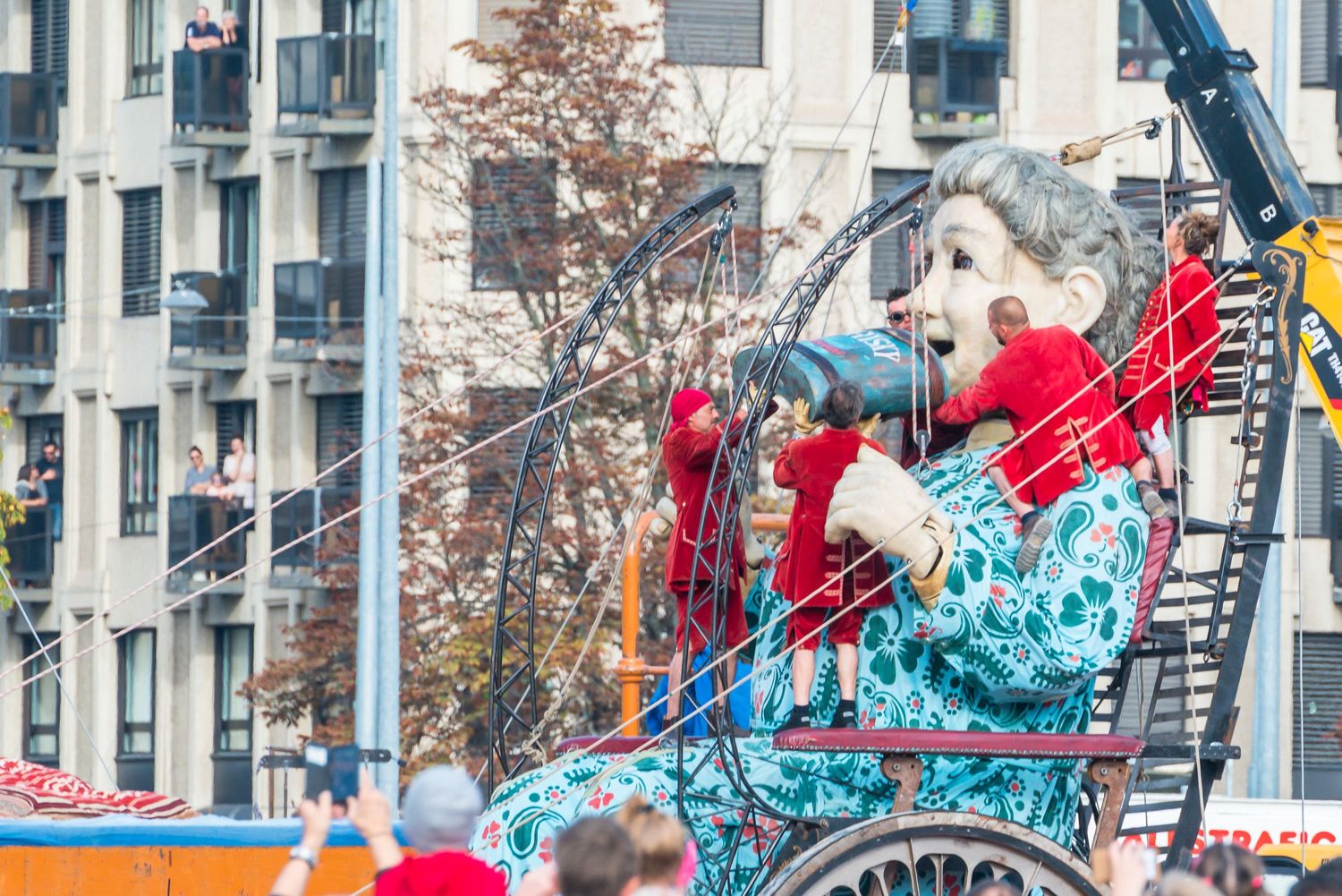 Colorful parade float featuring vibrant red and turquoise decorations moves down a city street during a festive celebration.