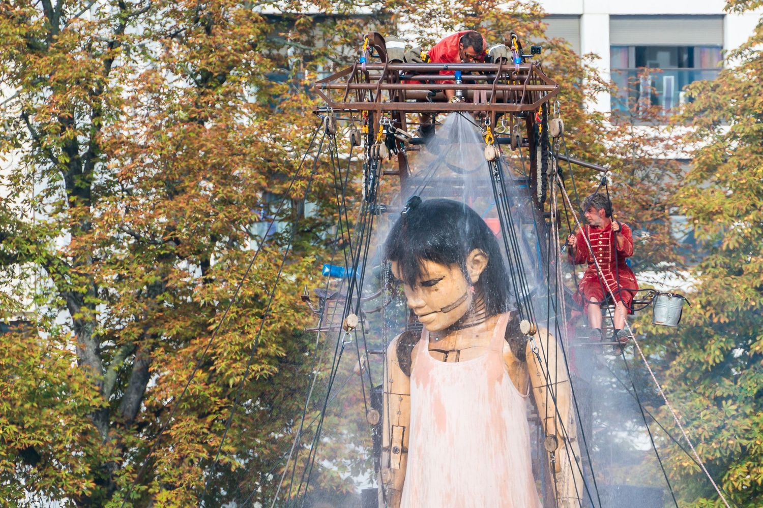 Traditional Asian marionette puppet displayed in front of autumn trees and buildings during festival performance.
