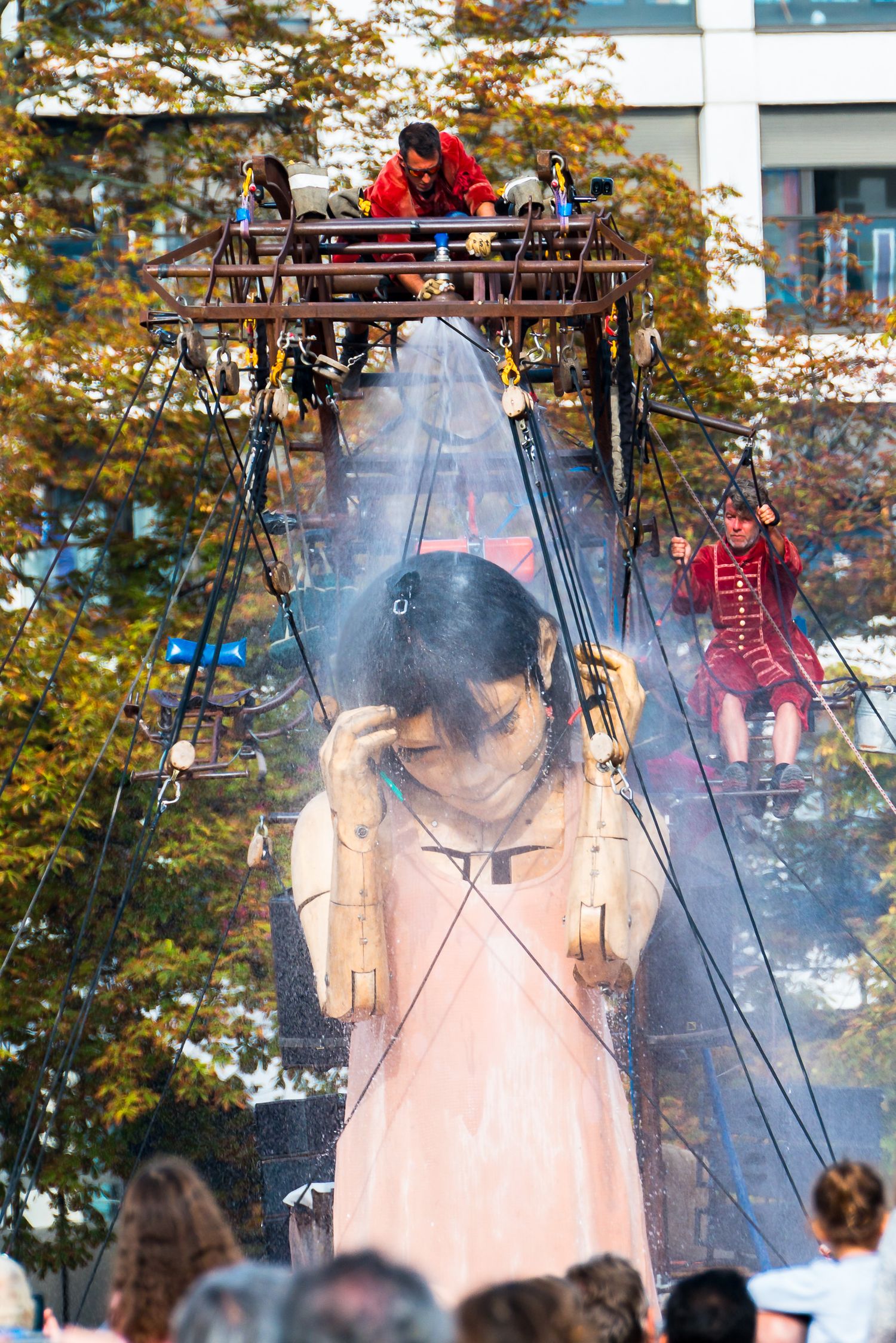 Giant puppet figure glows ethereally through smoke and fog while suspended by ropes during outdoor performance.