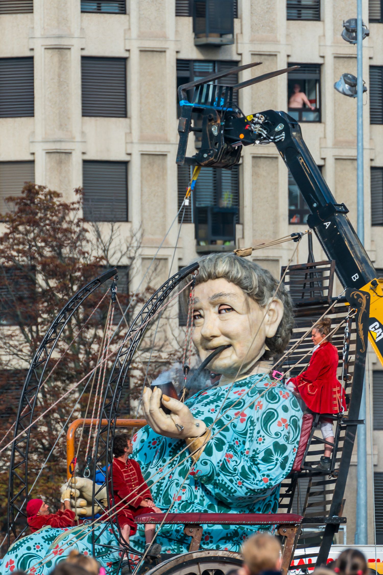 Large carnival puppet figure with turquoise robe and bright expression mounted on equipment during outdoor display.