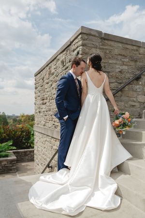 A romantic wedding couple embraces on a stone terrace with scenic views and a flowing white bridal gown.
