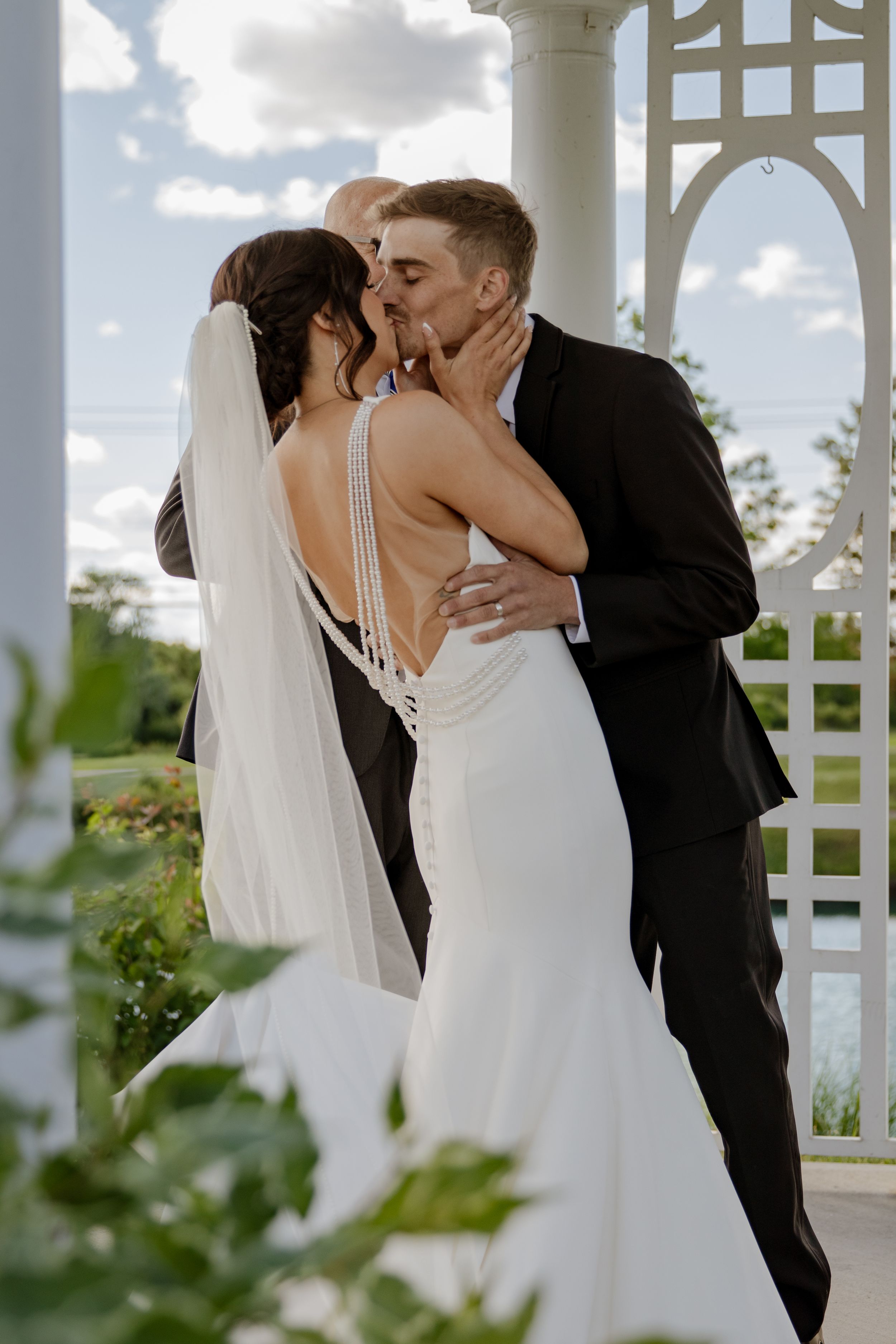 Wedding couple sharing a romantic kiss under an elegant white gazebo with a scenic outdoor backdrop.