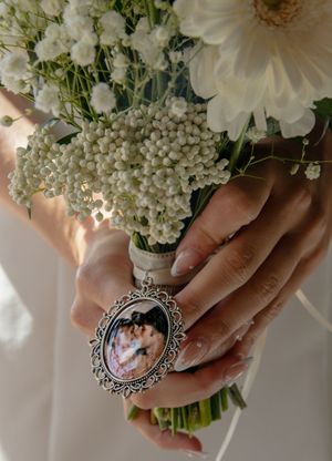 White floral wedding bouquet with delicate blooms and an ornate silver locket detail.