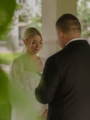 Intimate outdoor wedding ceremony moment captured through green foliage with natural lighting.