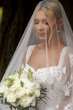 Elegant bridal portrait showing white veil, lace details and classic white rose bouquet.
