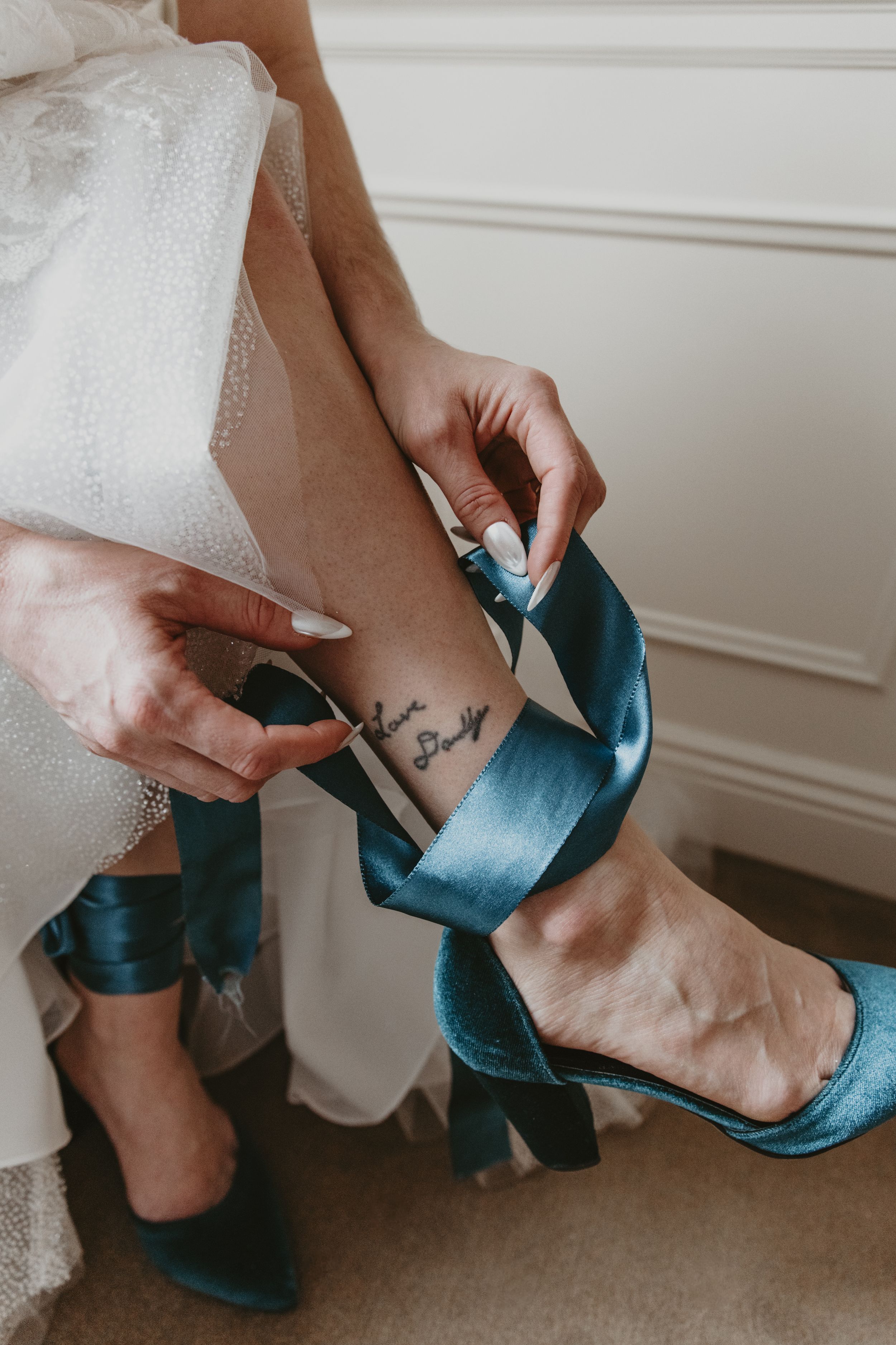 Close-up sequence showing hands putting on elegant teal blue high heels with white dress fabric in background.