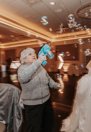 Guest in sparkly silver sweater blowing bubbles during wedding reception in luxurious venue.