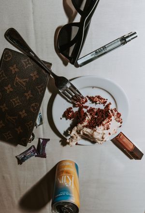 Flatlay of dessert plate with chocolate cake crumbs and various personal items on white tablecloth.